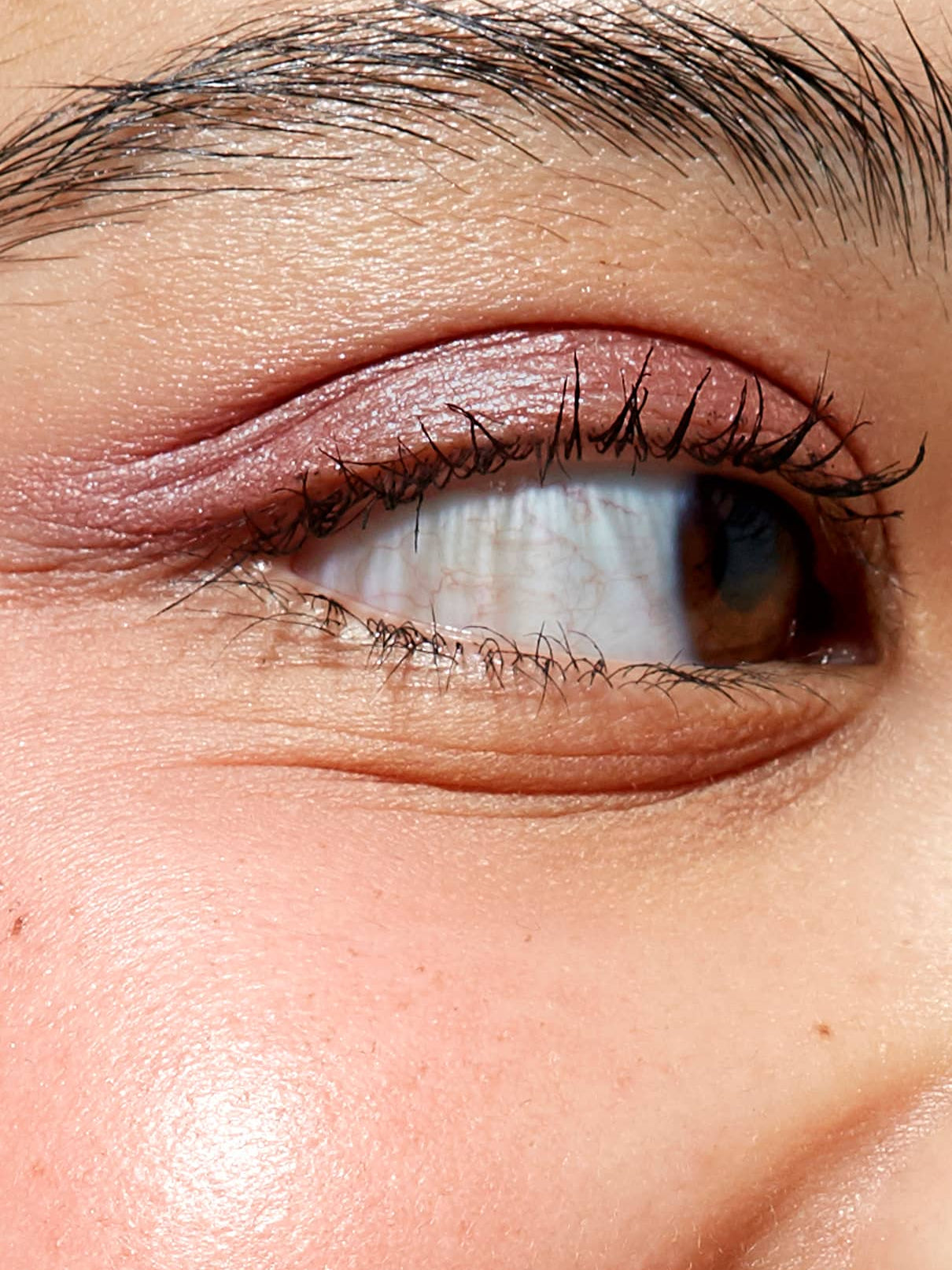 Nahaufnahme des seitlich blickenden Auges einer Person mit detaillierter Haut, Augenbrauen und Wimpern, die mit Visionist Nr. 01 - einem schimmernden Beerenton mit kühlem Unterton - veredelt wurden.