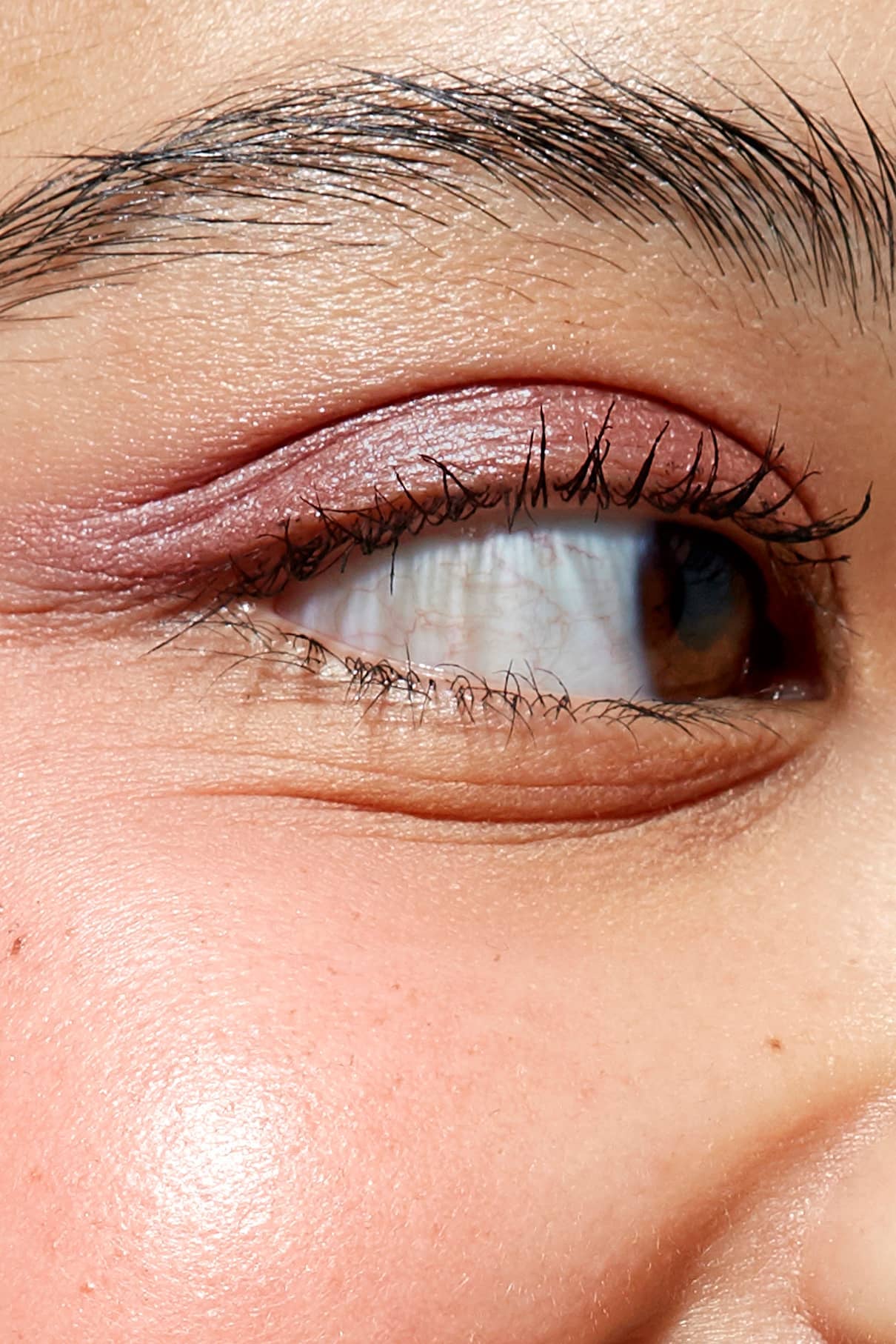 Nahaufnahme des Auges und der Augenbraue einer Person, mit Betonung der definierten Wimpern mit Mascara und einem leicht schimmernden Augenlid, das mit dem Eye Colour Set erstellt wurde. Die detaillierte Hauttextur ist sichtbar.