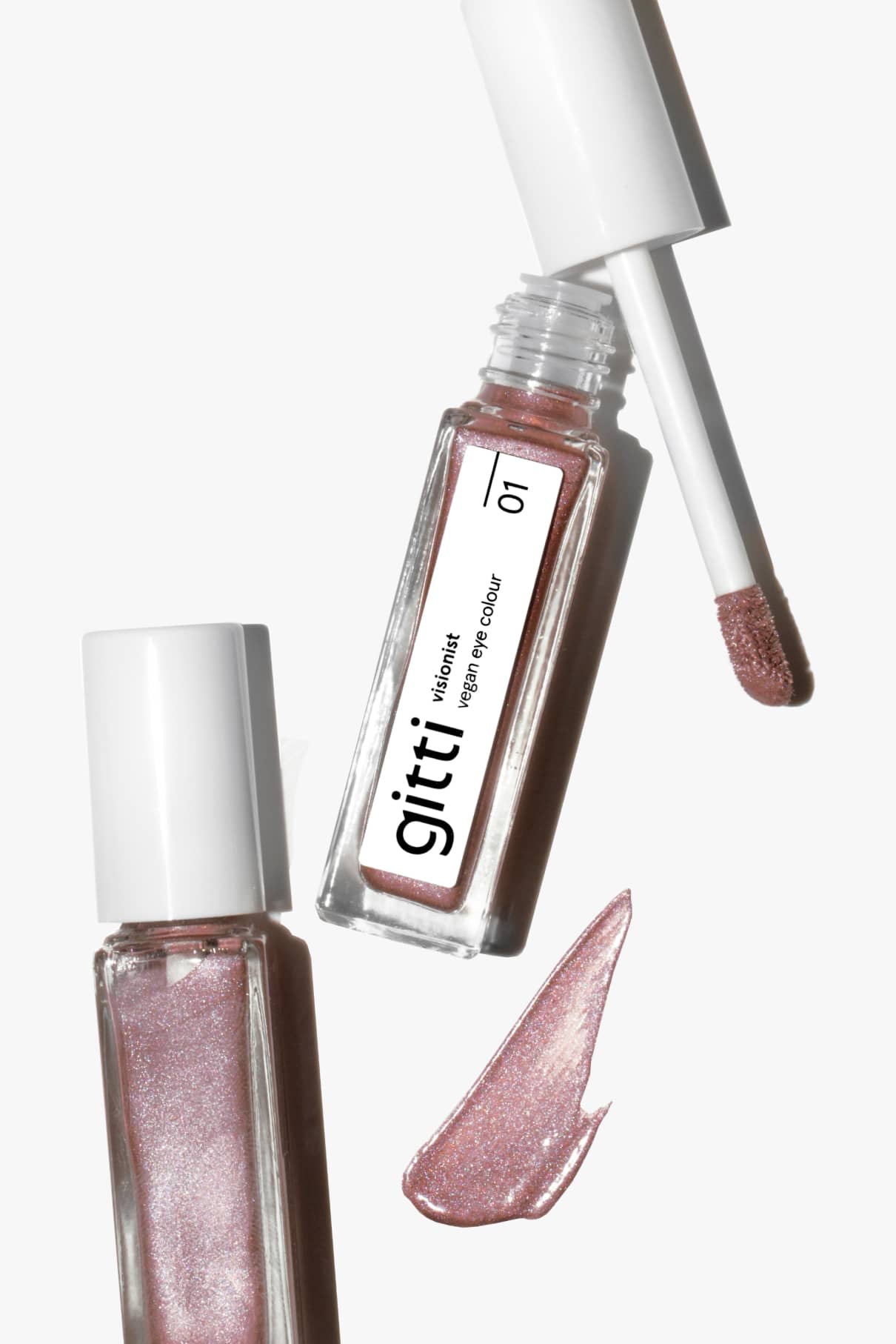 Zwei Tuben Visionist Nr. 01 rosa flüssige Augenfarbe mit kühlem Unterton, eine davon geöffnet mit dem Applikator und einem Spritzer des schimmernden Produkts auf einer weißen Fläche.