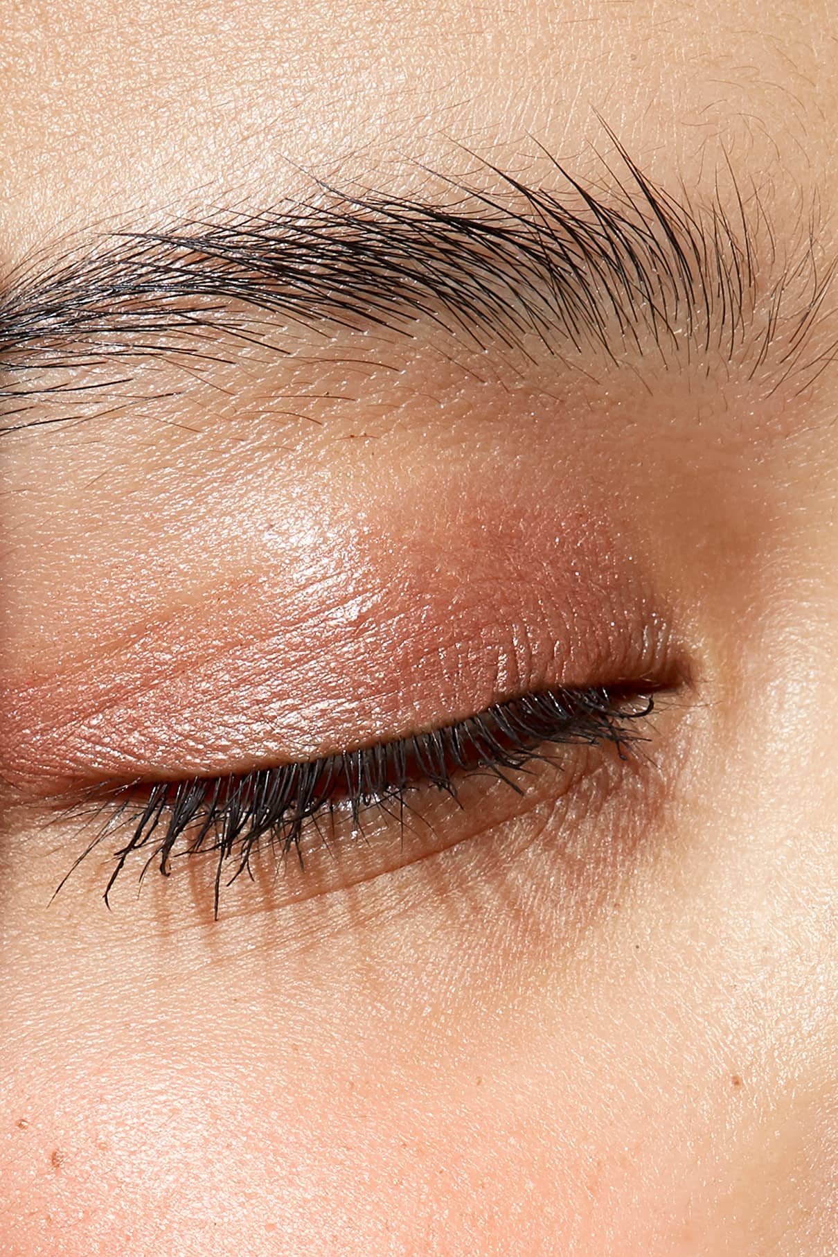 Nahaufnahme des geschlossenen Auges einer Person, Hervorhebung von Augenbraue, Wimpern und strukturierter Haut mit einem schimmernden Kupfer-Finish und neutralem Unterton mit Visionist Nr. 02.