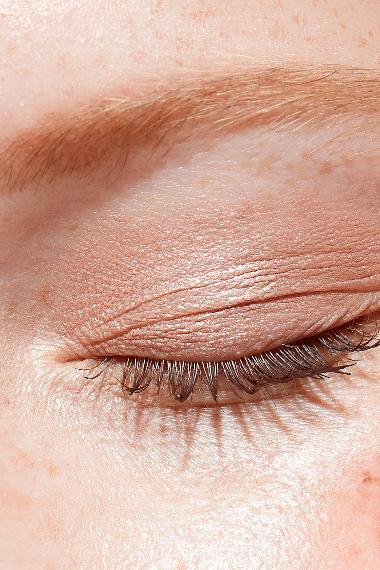 Nahaufnahme eines geschlossenen Auges mit Visionist Nr. 03, einem natürlichen braunen Lidschatten mit neutralem Unterton, gepaart mit braunen Augenbrauen, sichtbaren Wimpern und Sommersprossen.