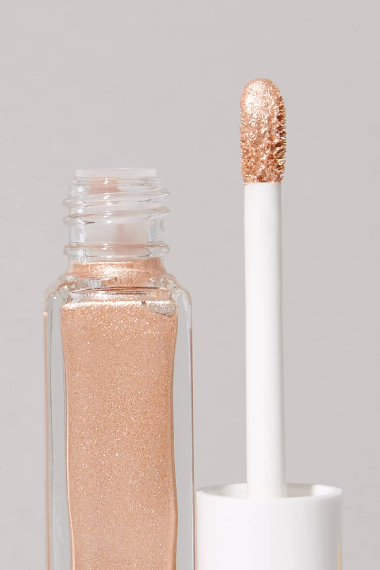Eine klare Tube des Visionist no. 03 schimmernden Nude Lipgloss mit weißem Applikatorstab steht aufrecht auf einem schlichten hellen Hintergrund. Der Gloss bietet schimmerndes Gold und einen neutralen Unterton für dezente Ausstrahlung.
