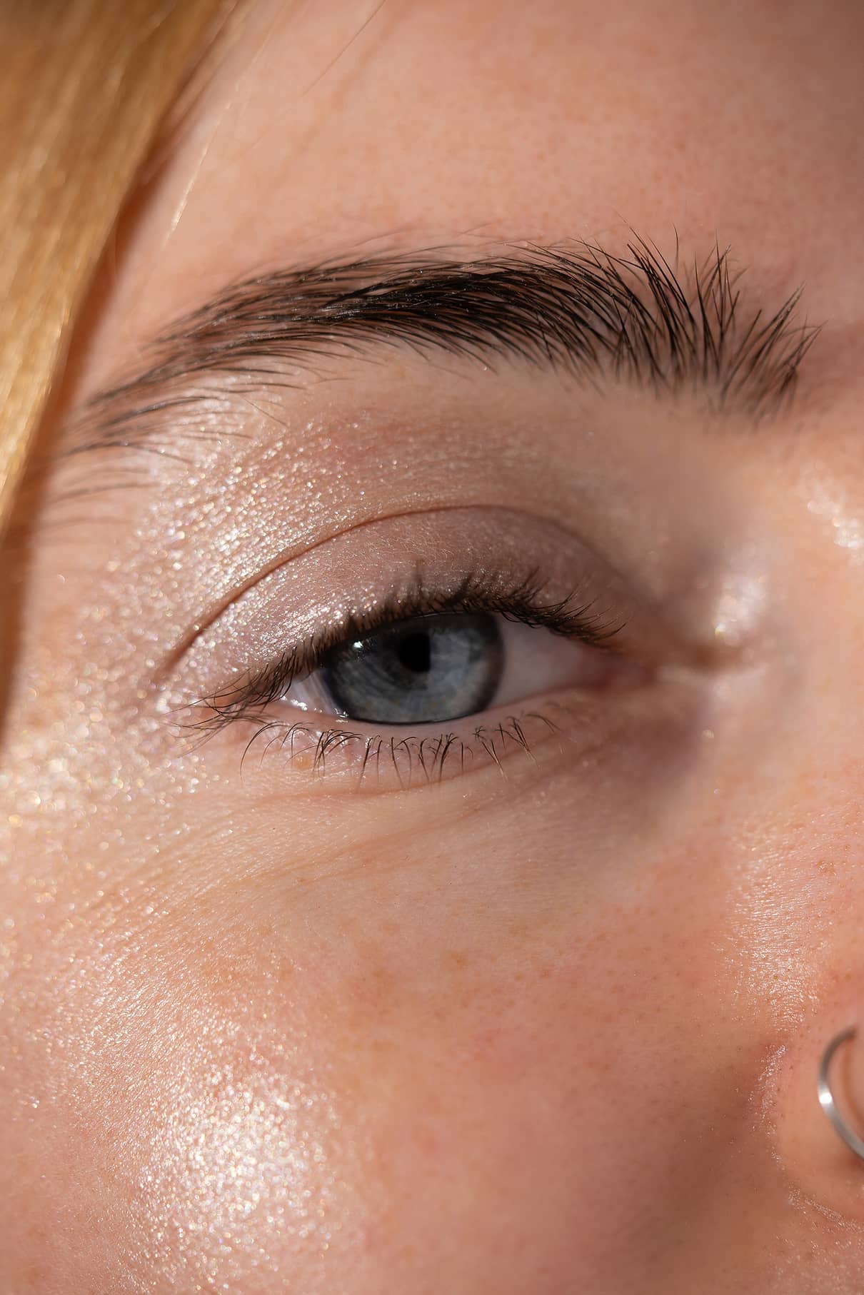 Nahaufnahme des blauen Auges einer Person, das mit Visionist Nr. 05 hervorgehoben wurde, mit Augenbraue, einem Teil der Nase mit silbernem Nasenring und detaillierter Hauttextur.