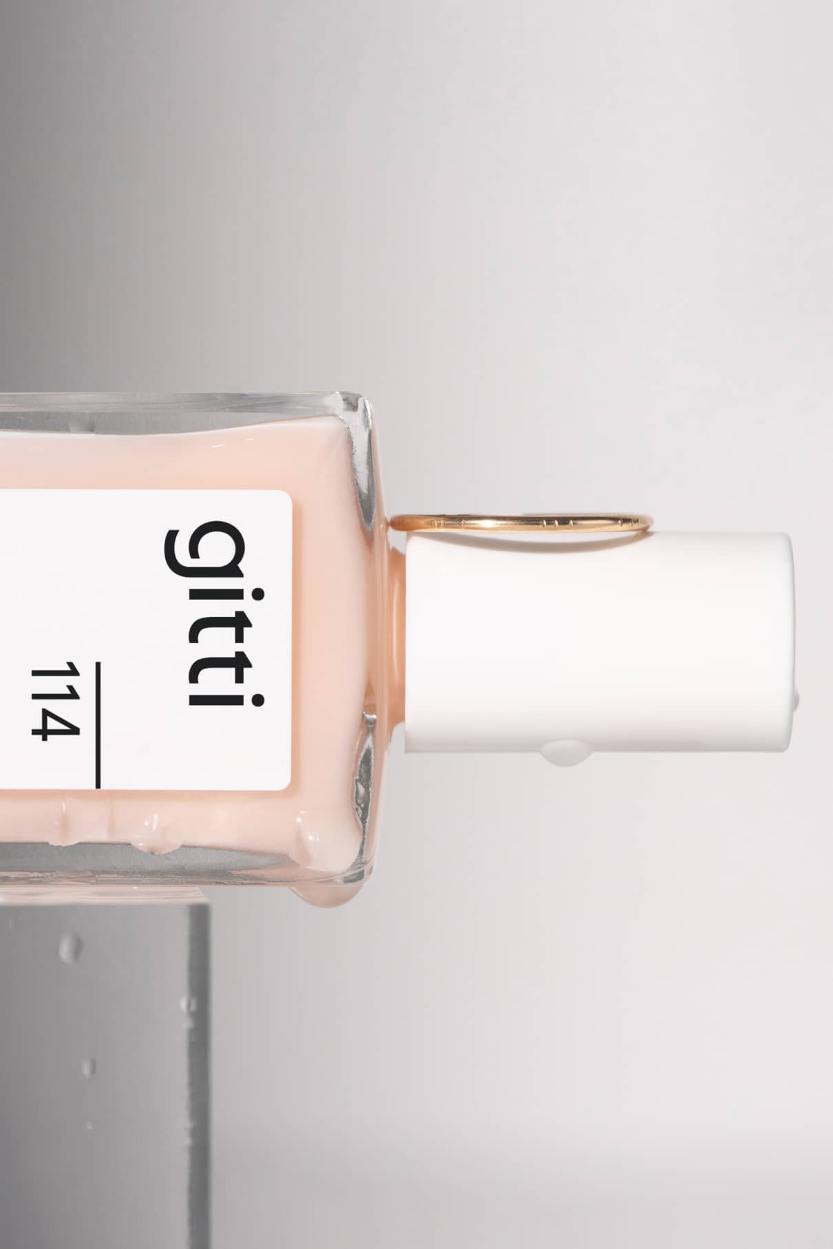 Eine Flasche Gitti-Nagellack mit der Aufschrift 114 liegt auf der Seite und hat eine weiße Kappe. Der Makaro Pontey Ring umgibt die Kappe und ergänzt den hellen, pfirsichfarbenen Nude-Ton des Lacks.
