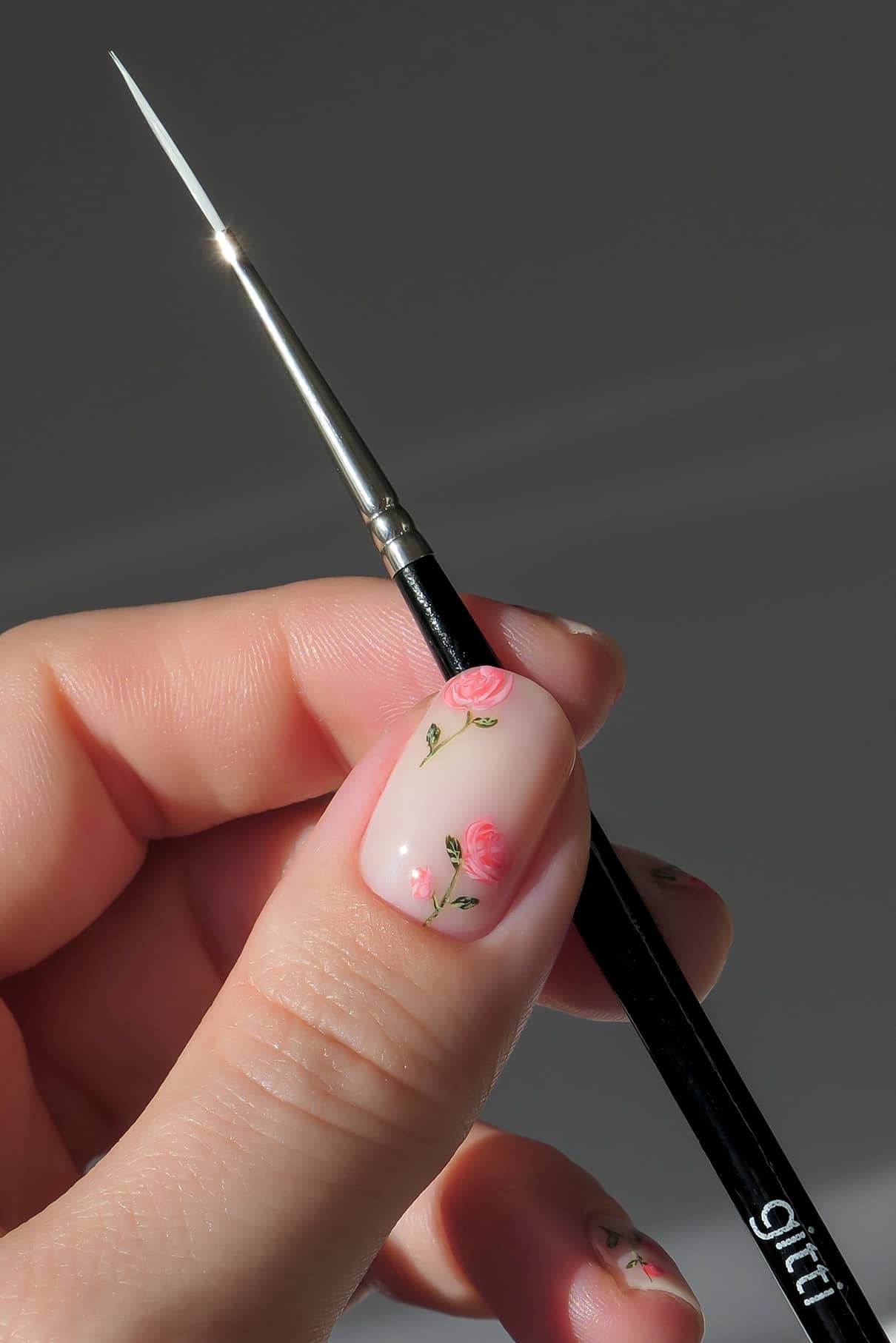 Eine Hand mit floraler Nailart hält einen dünnen Nail Art Pinsel aus dem Nail Art Duo von gitti vor einem schlichten Hintergrund.