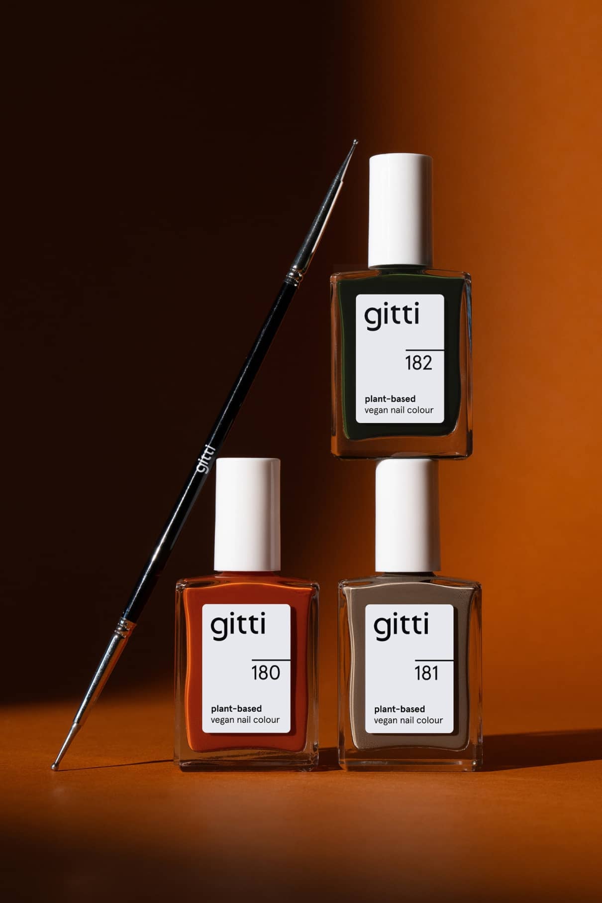 Das Nail Art Duo mit den pflanzlichen, veganen Nagelfarben von gitti in den Farbtönen 180, 181 und 182 und einem Nail Art Pinsel darauf bildet das perfekte Set vor einem braunen Hintergrund.