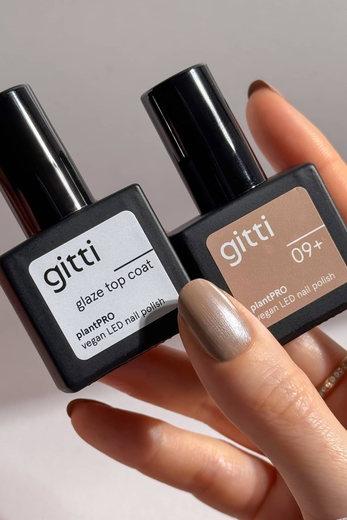 Eine Hand mit lackierten Nägeln hält zwei Flaschen aus dem plantPRO Essentials Set von Gitti-einer mit der Bezeichnung glaze top coat und der andere 09+-perfekt, um zusammen mit einem Base Coat eine makellose, vegane LED-Maniküre zu erhalten.