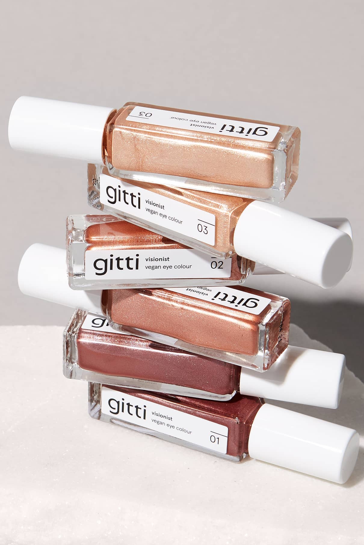 Vier Fläschchen aus dem Augenfarben-Set in verschiedenen Farbtönen sind vor einem neutralen Hintergrund gestapelt und eignen sich ideal zur Ergänzung Ihrer Make-up-Sammlung.