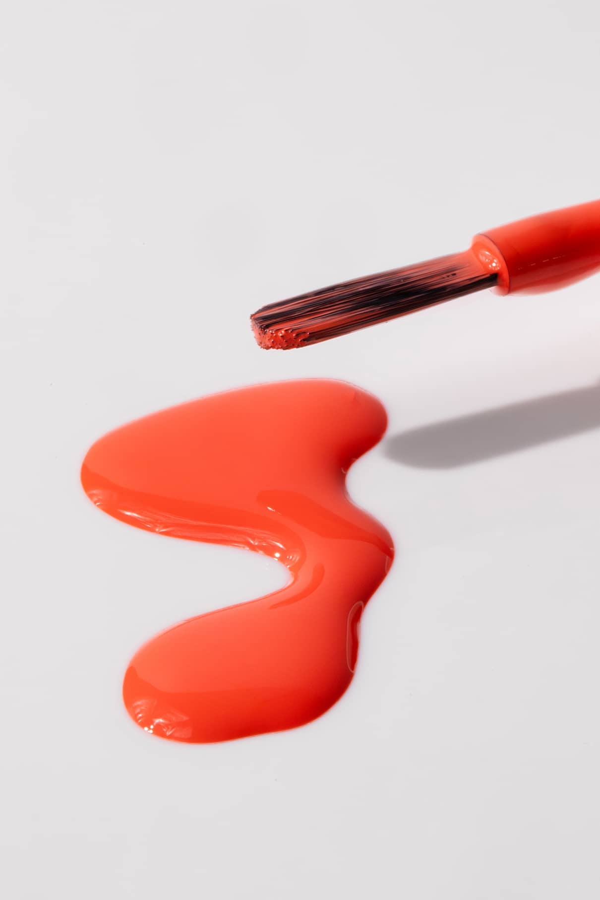 Der gitti kids no. 02 Nagellackpinsel in leuchtendem Rot ruht über einer Pfütze aus verschüttetem roten Lack auf einer weißen Fläche.