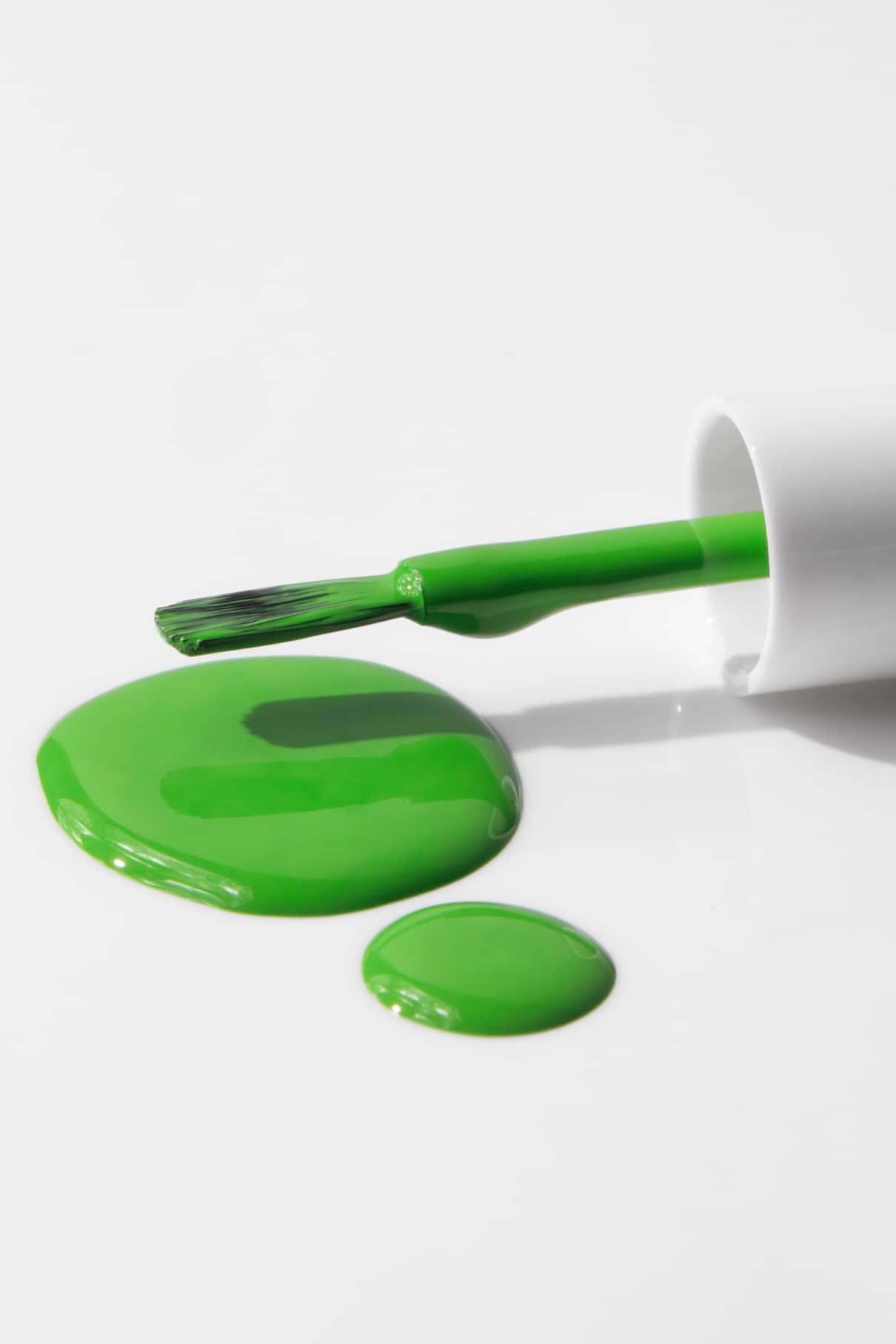 Ein Pinsel von gitti kids no. 04 grüner Nagellack liegt neben zwei Pfützen verschütteten grünen Lacks auf einer weißen Fläche.