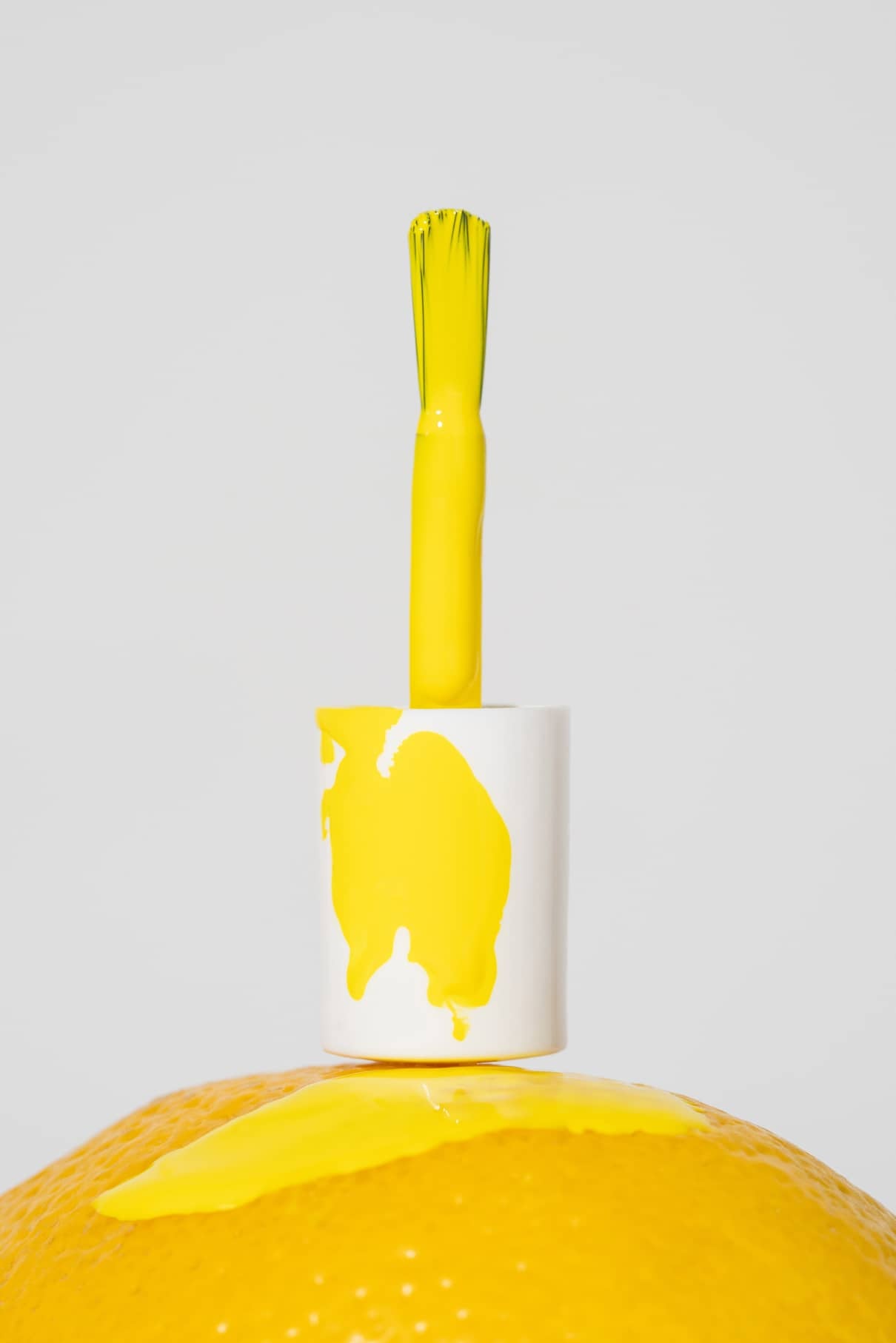 Eine Flasche gitti kids no. 06 Nagellack steht aufrecht mit seiner Kappe auf einer gelben Fläche und verschüttetem gelben Lack und unterstreicht diese kinderfreundliche Nagelfarbe perfekt für die Kleinen.