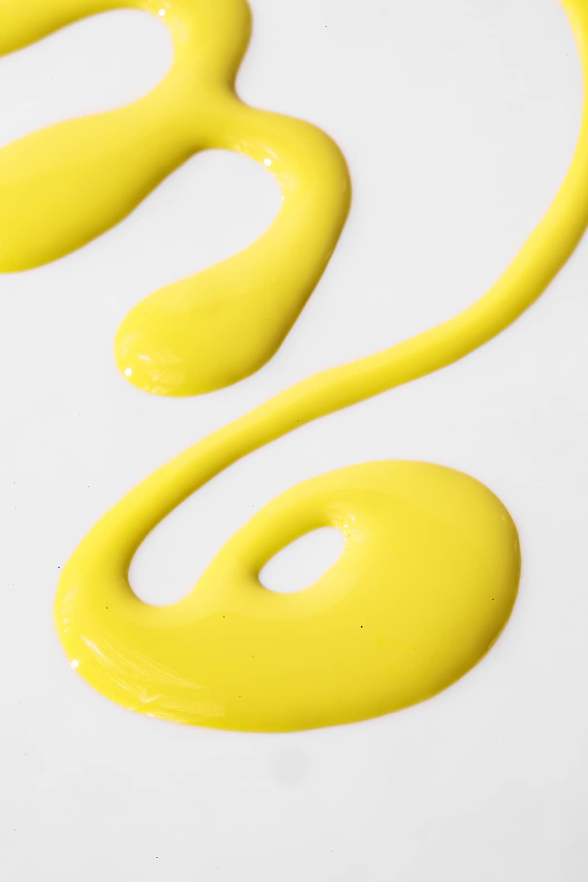Ein Strudel und geschwungene Linien aus gelber gitti kids no. 06 kindersichere Nagellackfarbe sind auf einer weißen Fläche verteilt.