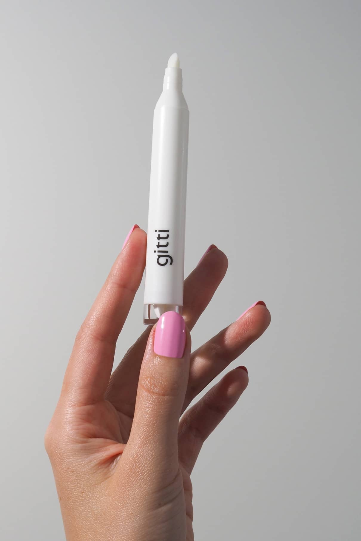 Eine Hand mit rosafarbenem Nagellack hält ein weißes stiftförmiges Produkt mit der Aufschrift gitti Perfect Finish Set, das eine schnell trocknende Lösung enthält, vor einem schlichten hellen Hintergrund.