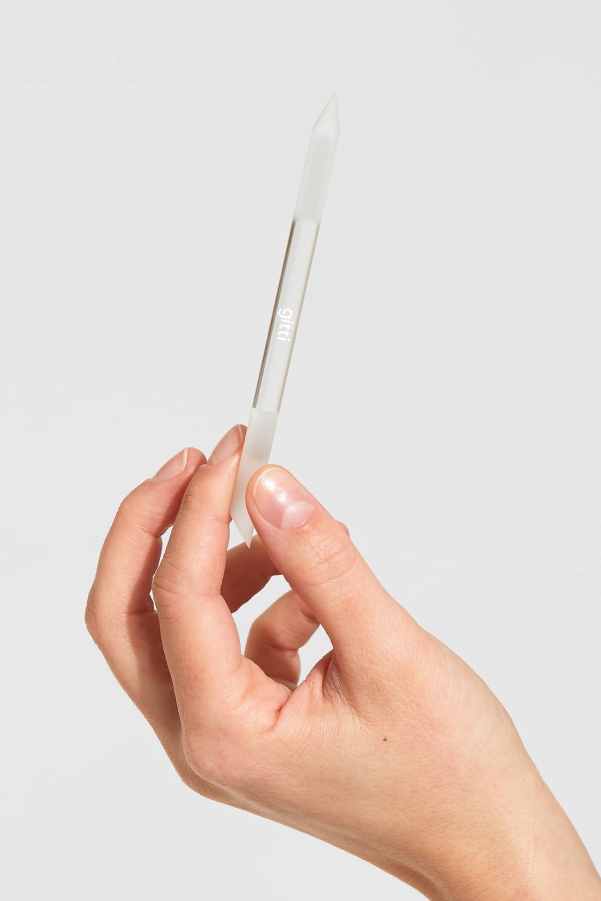 Eine Hand hält einen hochwertigen, doppelseitigen Nagelhautschieber vor einem schlichten, hellen Hintergrund.