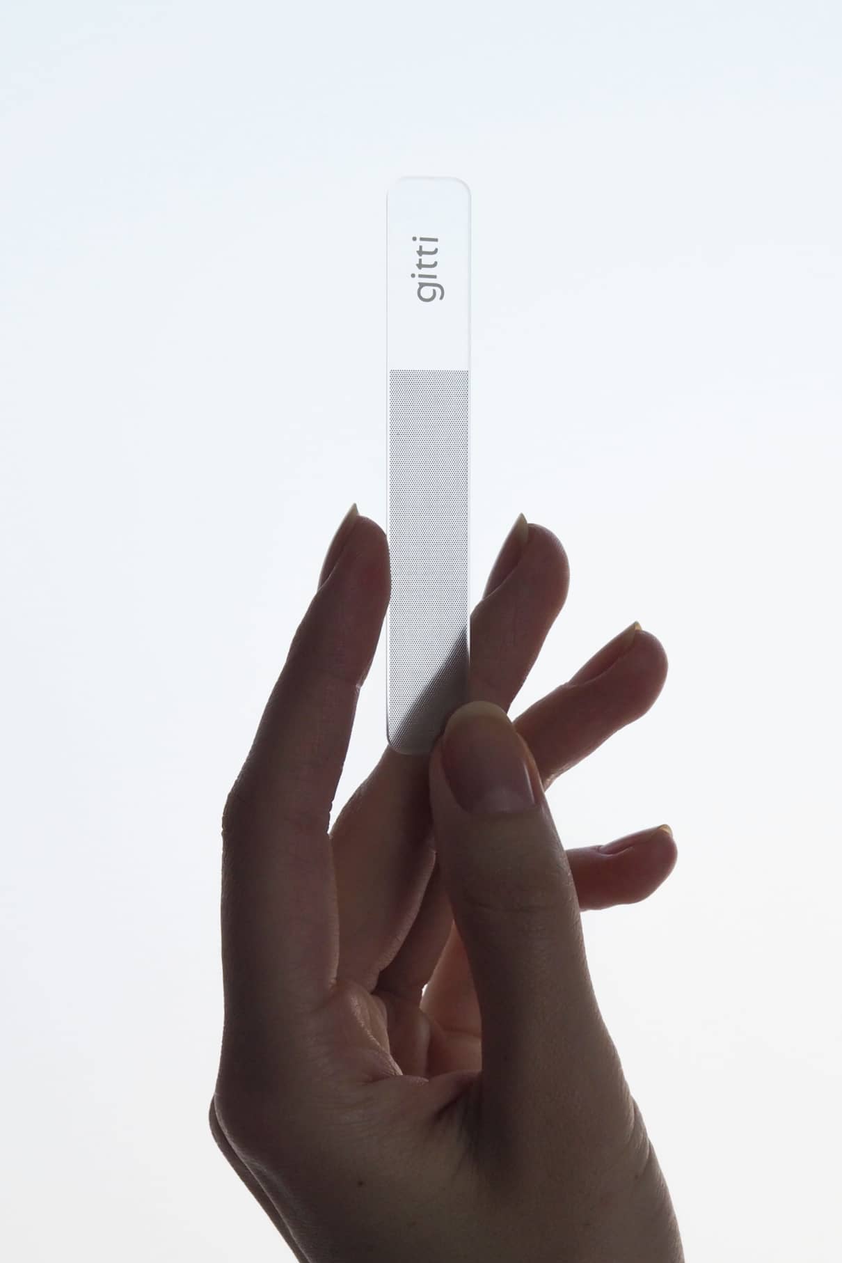 Eine Hand hält einen Nagelbuffer mit der Aufschrift gitti vor einem schlichten, hellen Hintergrund, ideal für glänzende Nägel.