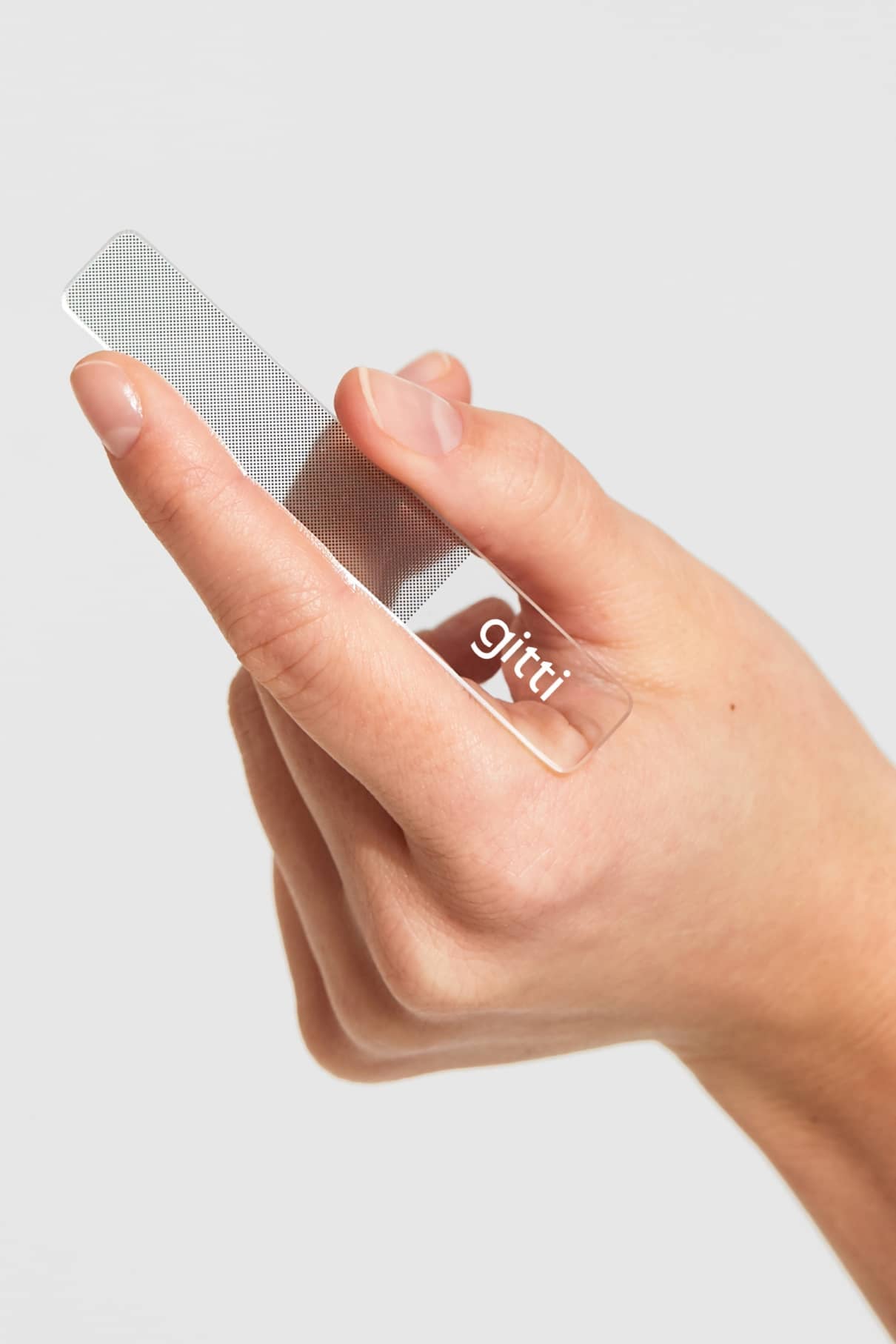 Eine Hand hält den gitti Nagelbuffer, einen durchsichtigen Nagelbuffer mit dem gitti-Logo, vor einem schlichten Hintergrund - ideal für glänzende Nägel.