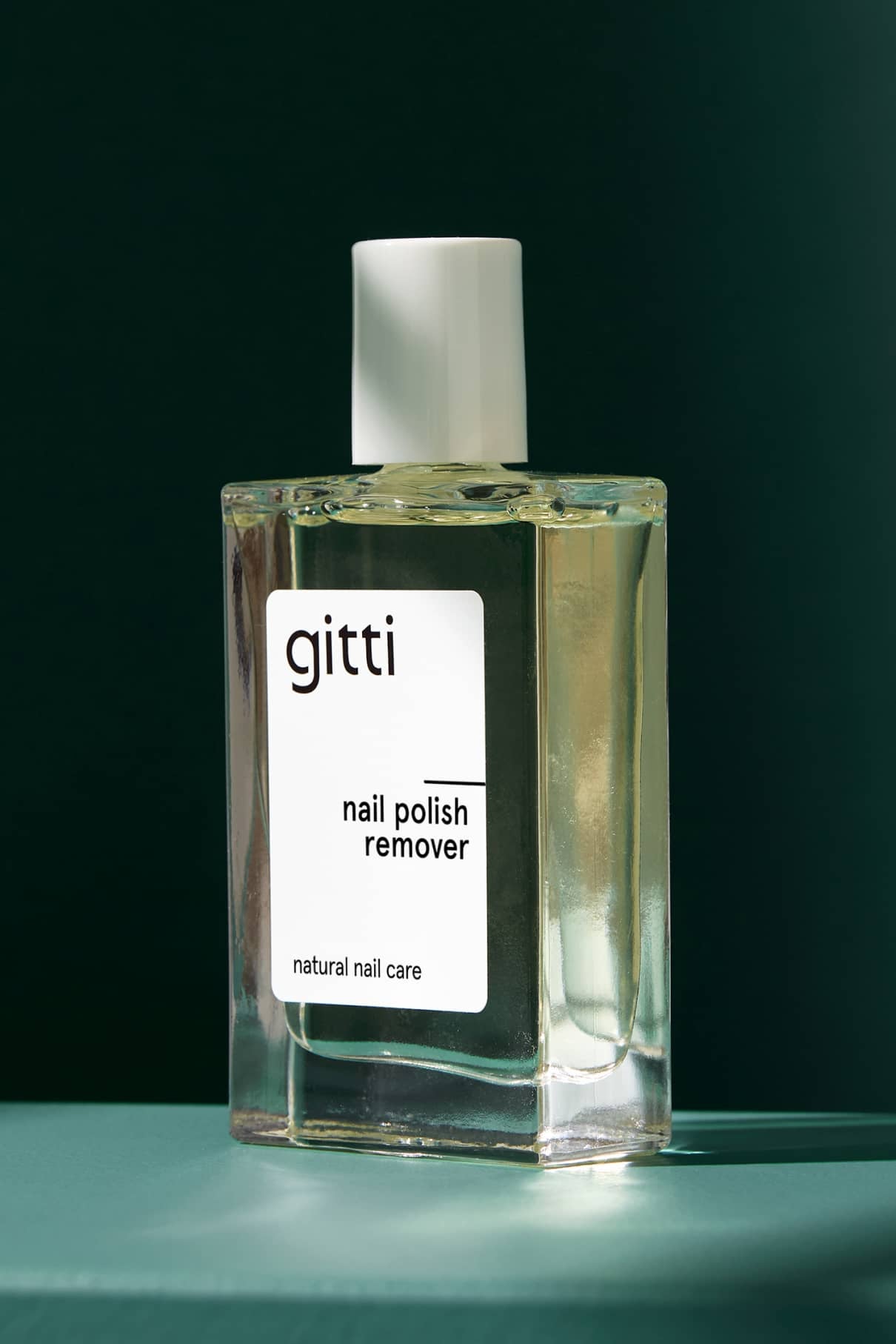 Eine klare, quadratische Flasche Nagellackentferner für die natürliche Nagelpflege wird vor einem grünen Hintergrund präsentiert, der den angenehmen Duft hervorhebt.
