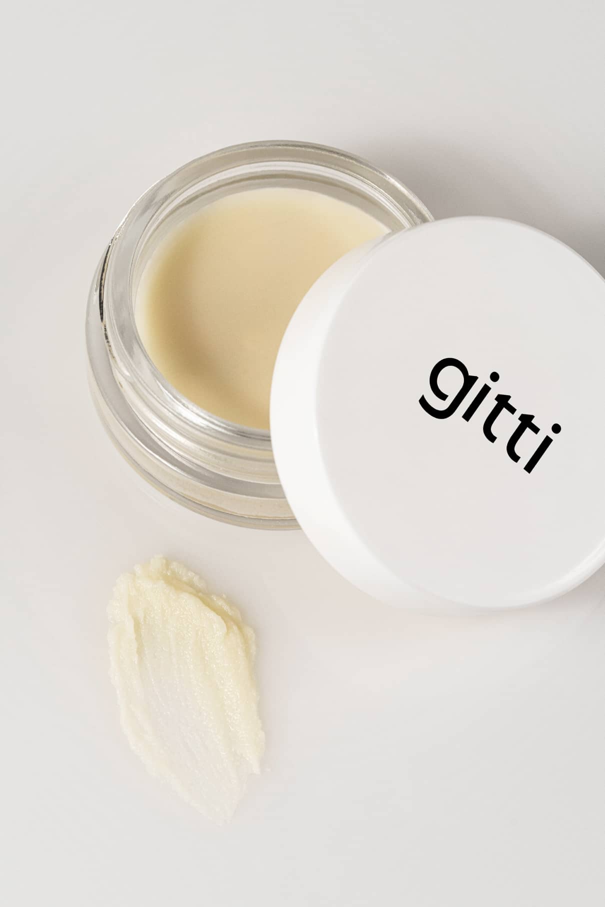 Ein kleines offenes Töpfchen mit einem weißen Deckel mit der Aufschrift gitti steht neben einem Klecks der Creme auf einer weißen Fläche - perfekt für die sanfte Entfernung der Pflanzenfarben von Plant Trio.