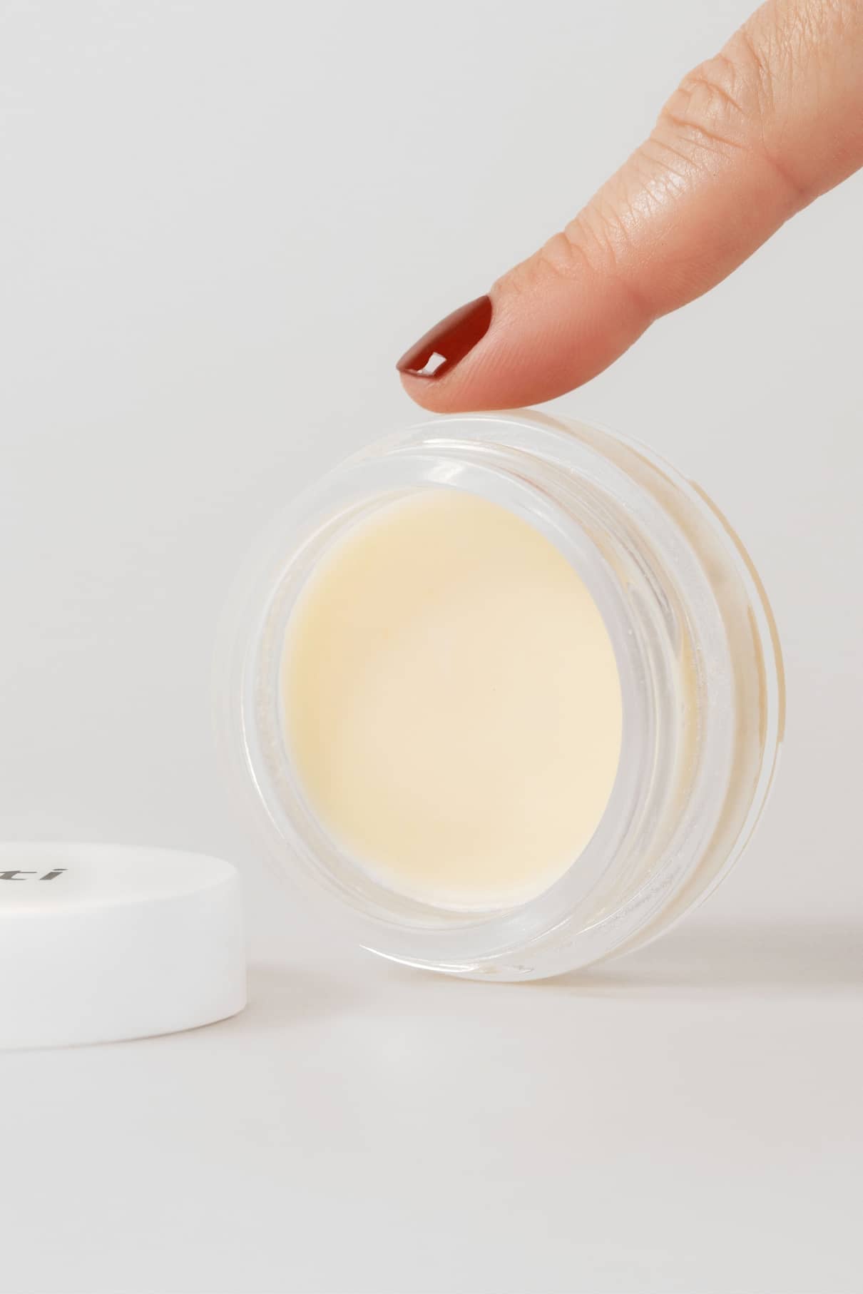 Eine Hand mit lackierten Nägeln greift nach einer offenen Dose Nagellackentferner Balsam, der eine sanfte und wirksame Methode zum Entfernen von Nagellack bietet.