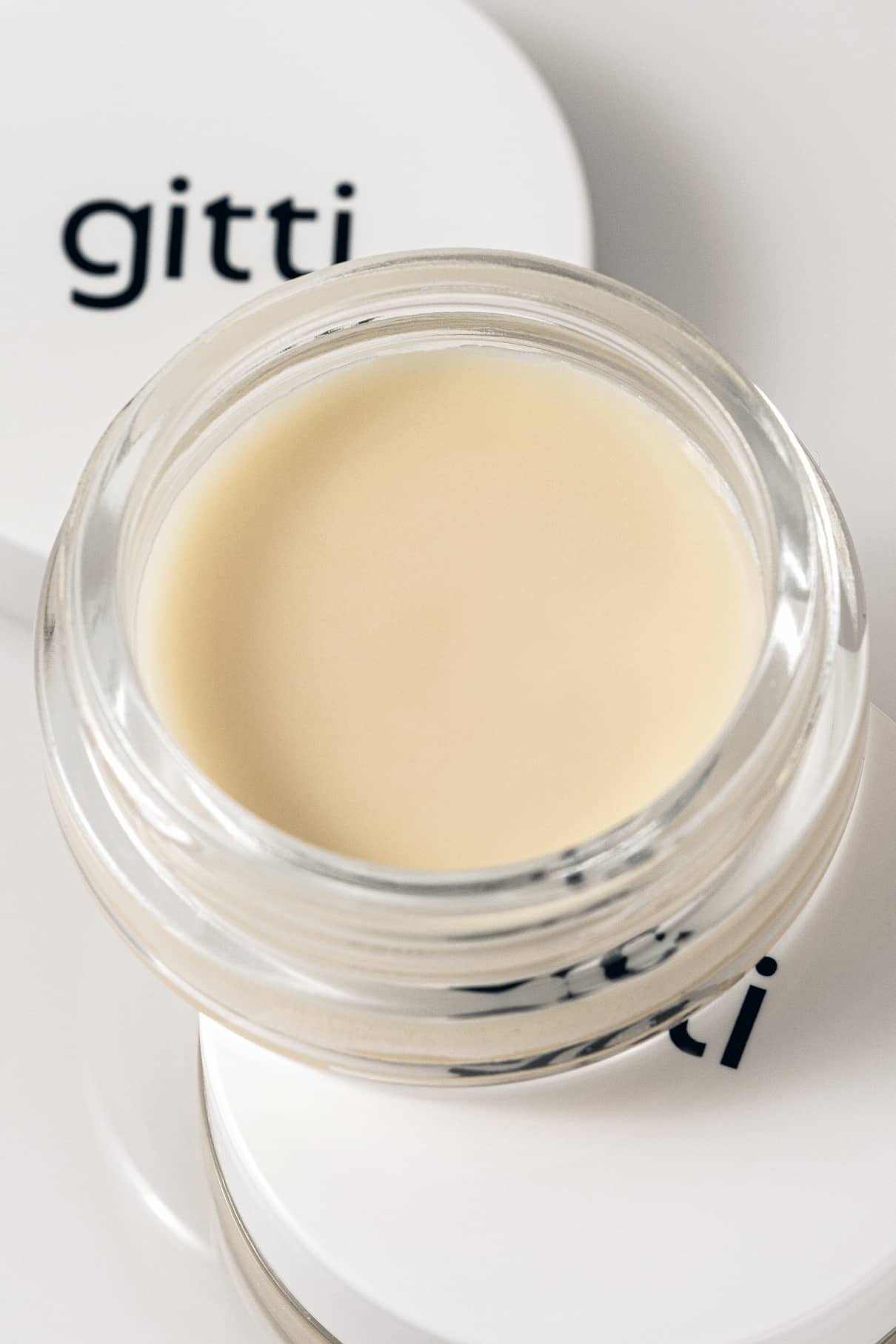Ein kleiner Glastiegel Nagellackentferner Balsam, gefüllt mit hellbeigem, cremigem Nagellackentferner, steht neben einem weißen Deckel mit der Aufschrift gitti.