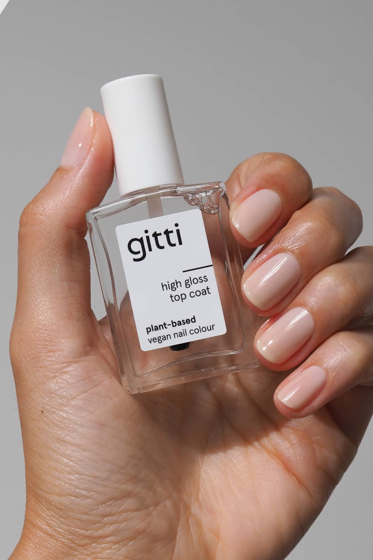 Eine Hand mit ordentlich manikürten Nägeln hält eine Flasche High Gloss Top Coat, der für seine pflanzliche, vegane Formel und sein atemberaubendes Hochglanzfinish bekannt ist.