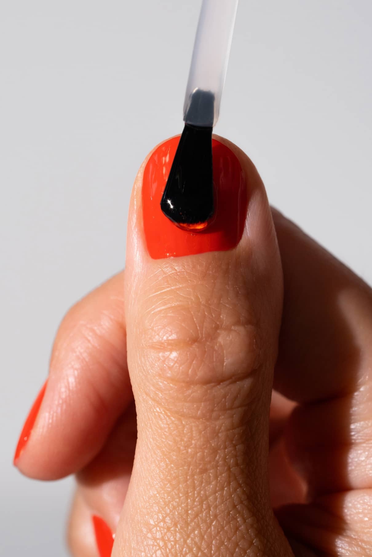 Bei einer Hand mit rotem Nagellack wird mit einem Pinsel High Gloss Top Coat auf den Daumennagel aufgetragen, der für ein glänzendes Finish sorgt und die Maniküre perfekt macht.
