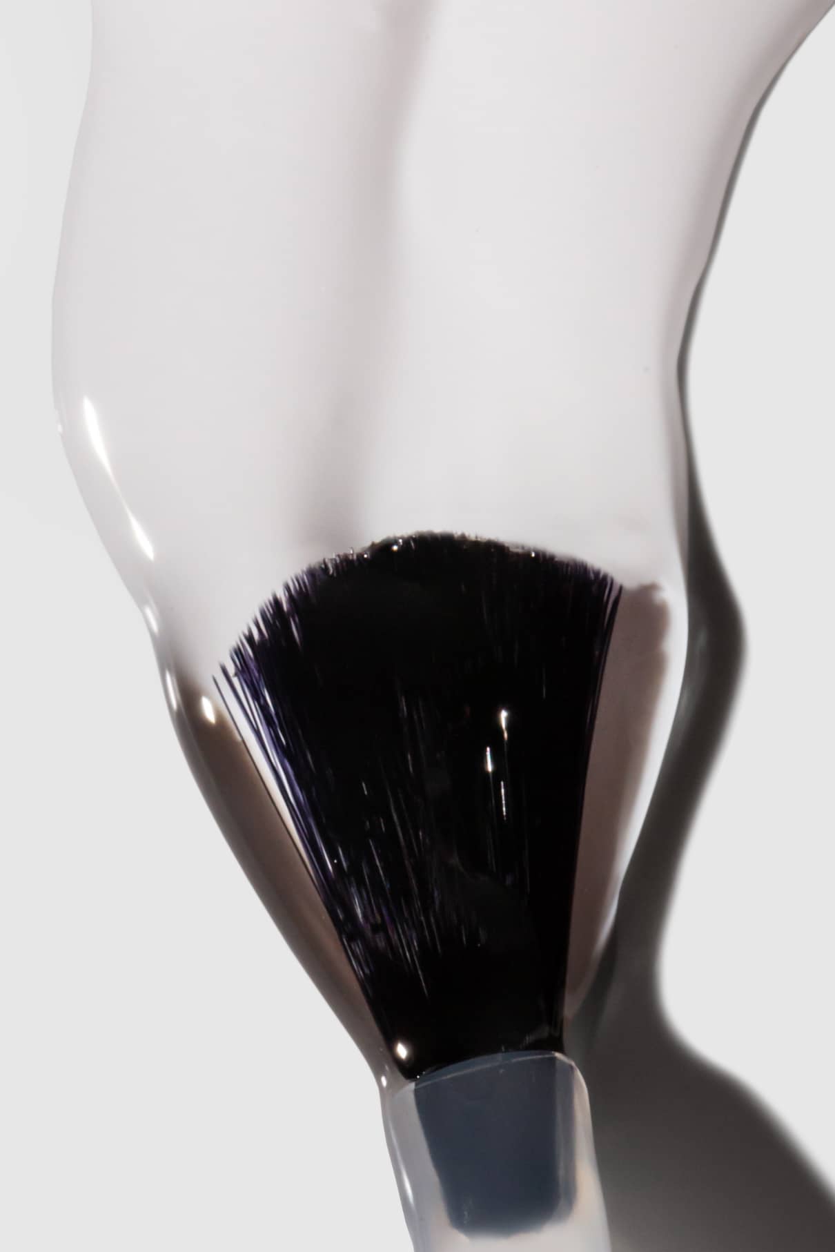Nahaufnahme eines Make-up-Pinsels, der den High Gloss Top Coat aufträgt und eine weiße Schicht auf einer glatten Oberfläche aufträgt, um ein makelloses, hochglänzendes Finish zu erzielen.