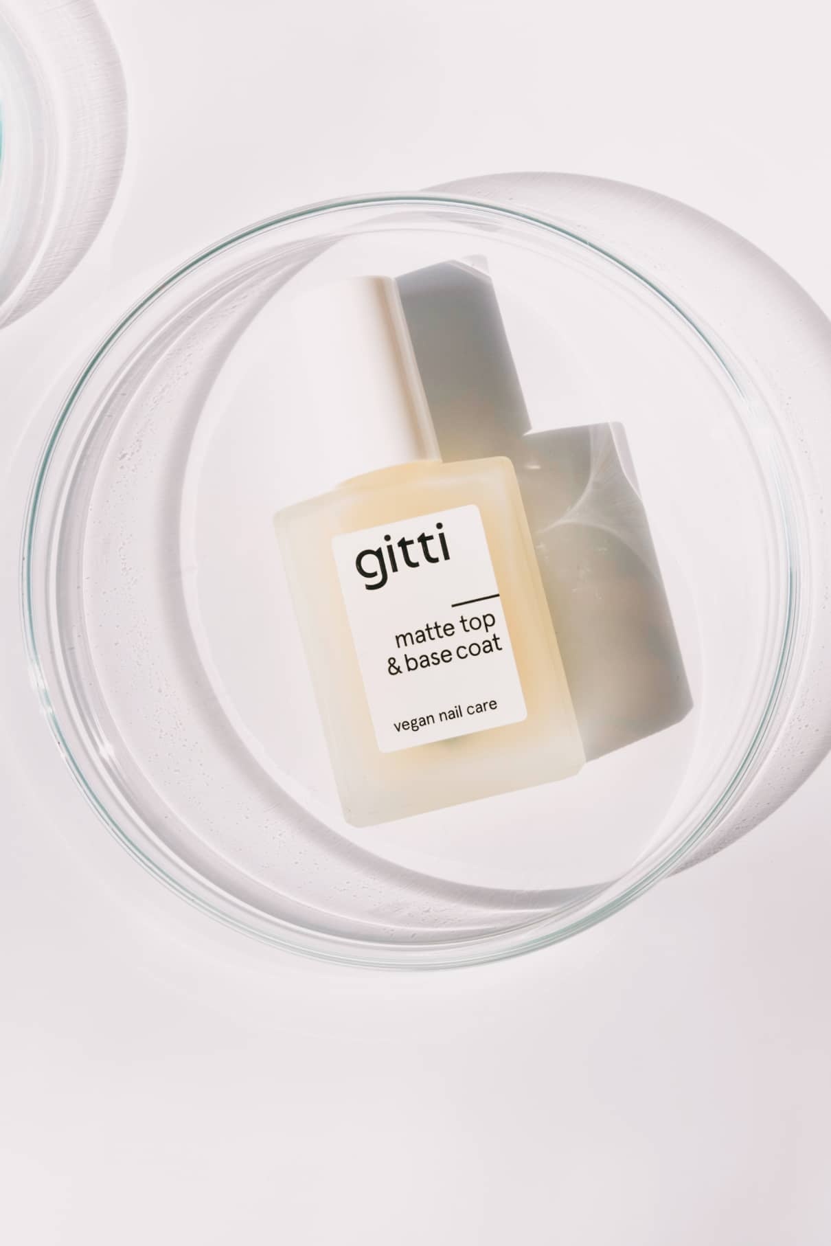 Eine Flasche Matte Top & Base Coat vegane Nagelpflege für zusätzlichen Halt und ein mattes Finish befindet sich in einer klaren Glasschale auf weißem Hintergrund.