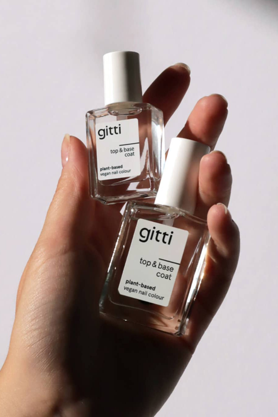 Eine Hand hält zwei Flaschen aus dem Mini Getaway Set - Gitti's pflanzlicher, veganer 2-in-1 Top&Base Coat in praktischer Mini-Größe - vor einem hellen Hintergrund, perfekt für Ihr nächstes Reiseset.
