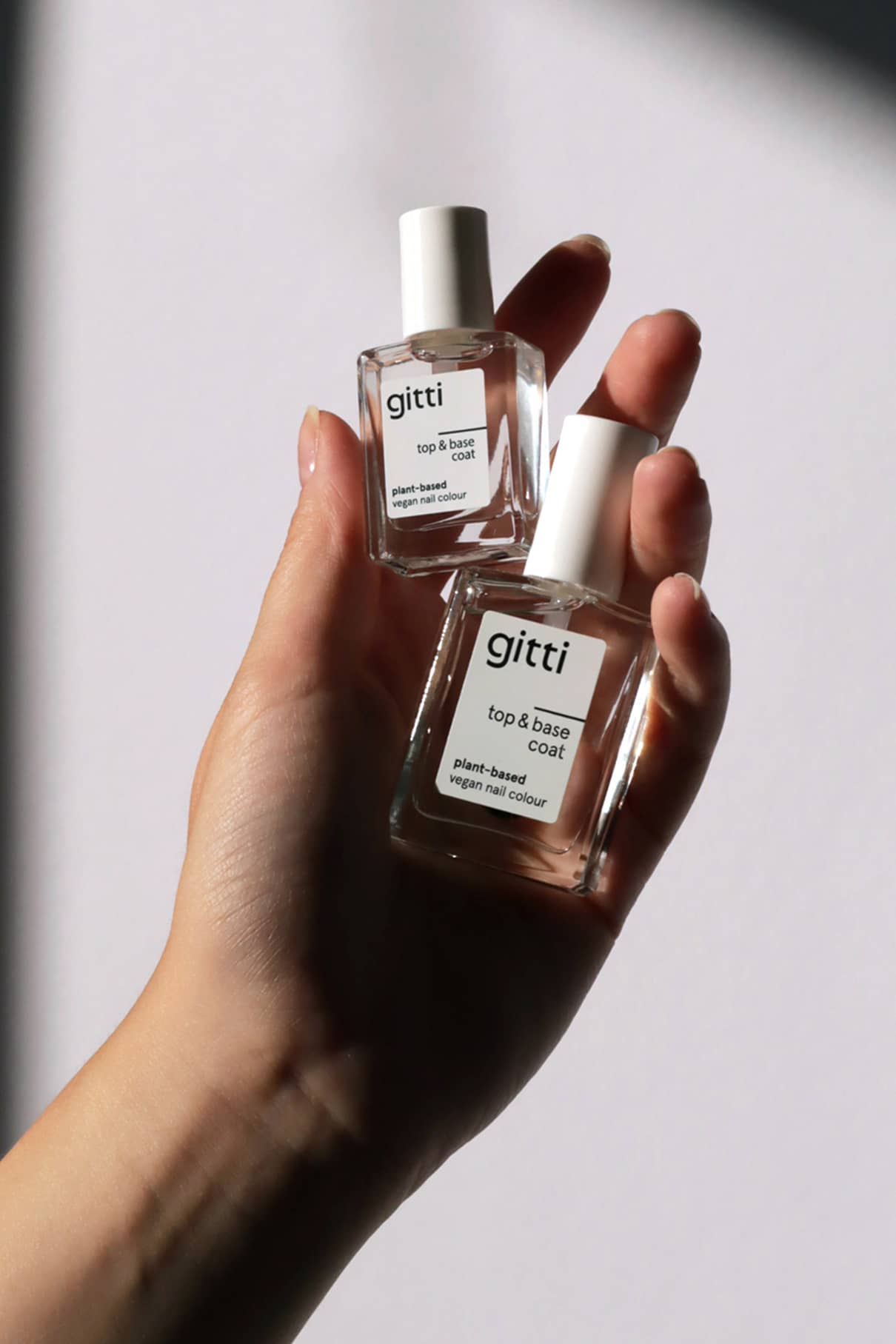 Eine Hand hält zwei Flaschen Mini Plant-based Top & Base Coat vor einem schlichten hellen Hintergrund.
