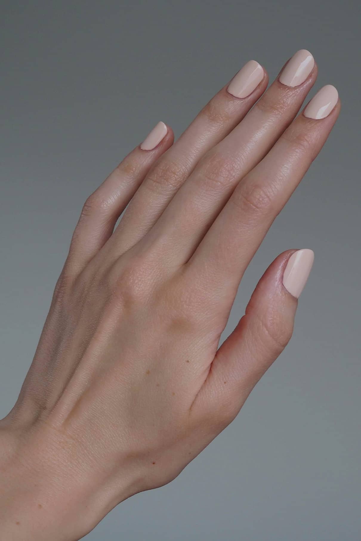 Eine Nahaufnahme zeigt eine hellhäutige Hand mit sauber manikürten, nudefarbenen Nägeln unter Verwendung des Top & Base Coat Duos - perfekt für kreative Looks - vor einem schlichten grauen Hintergrund.