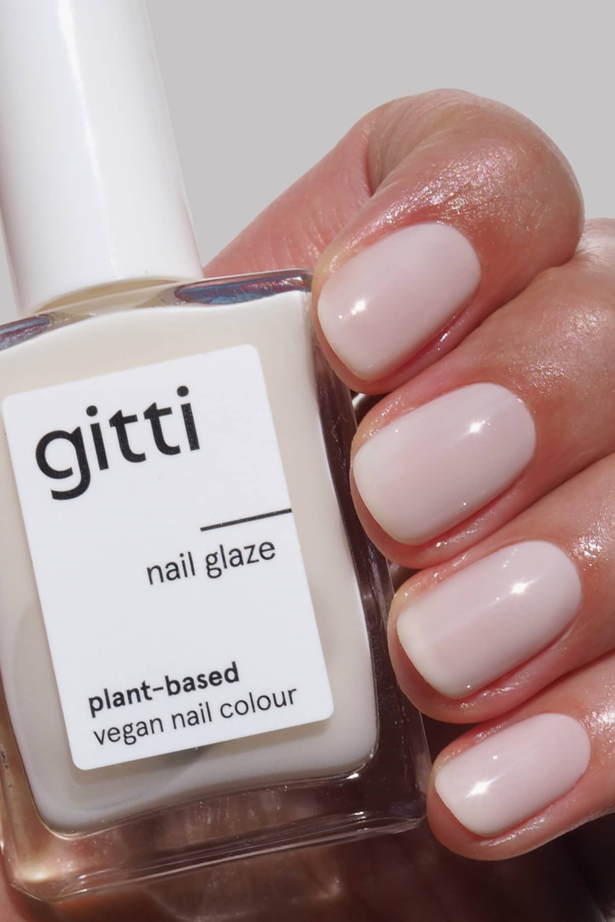 Eine Hand mit kurzen, sauber manikürten Nägeln, die in einem milchig weißen, halbtransparenten Farbton lackiert sind, hält eine Flasche Nail Glaze.