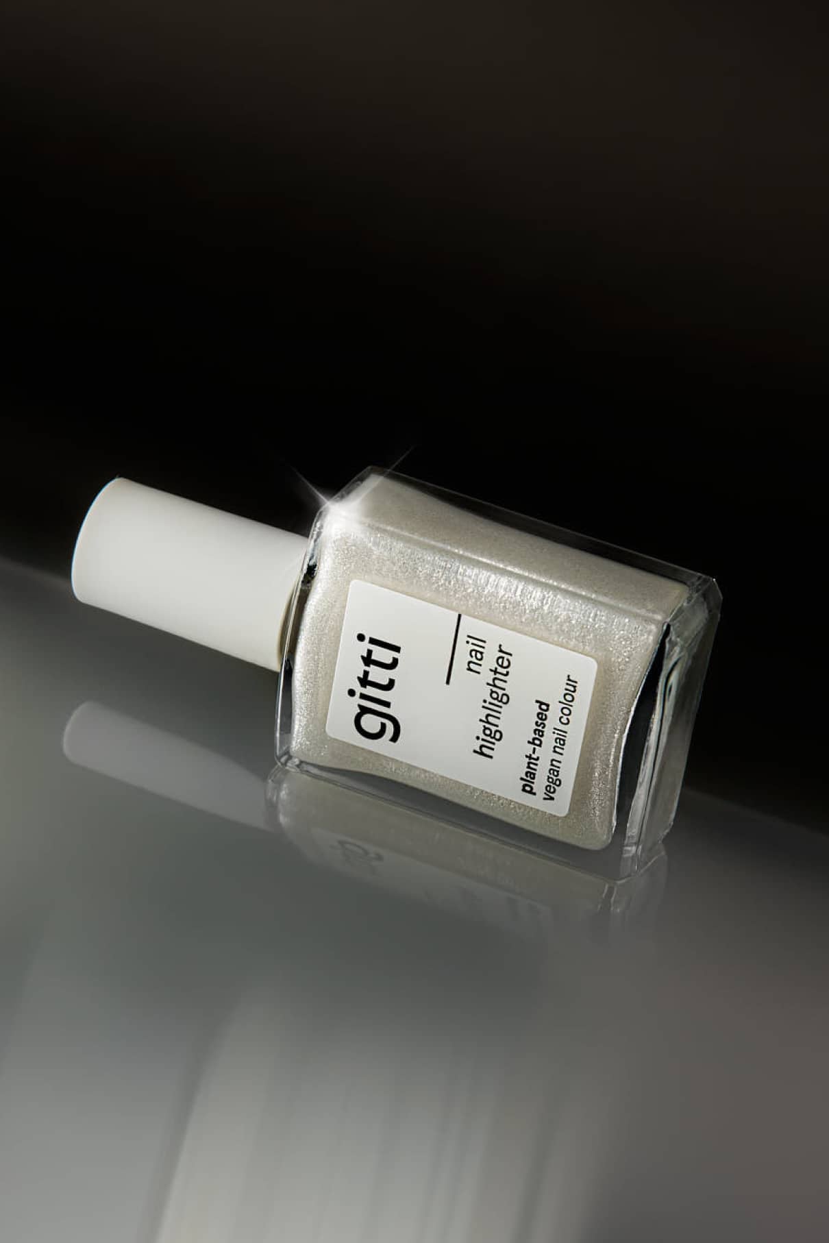 Ein Fläschchen Nail Highlighter mit weißer Kappe liegt auf der Seite vor einem unscharfen, dunklen Hintergrund und hebt das schimmernde Finish für Ihre Nägel hervor.