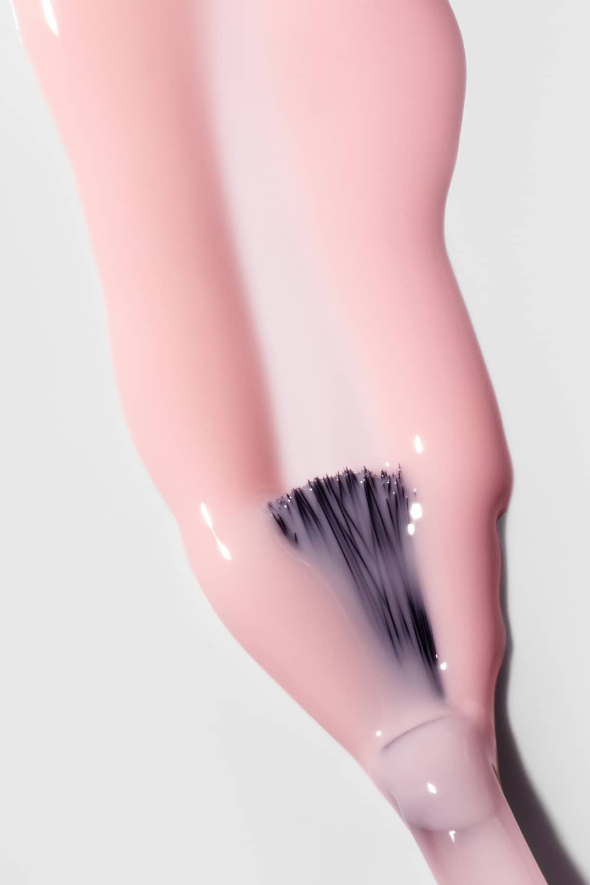 Eine Nahaufnahme eines Nail Tint Pinsels, der einen milchigen, hellrosa Farbton aufträgt, der den Nägeln ein zartes, sanftes Rosa verleiht.