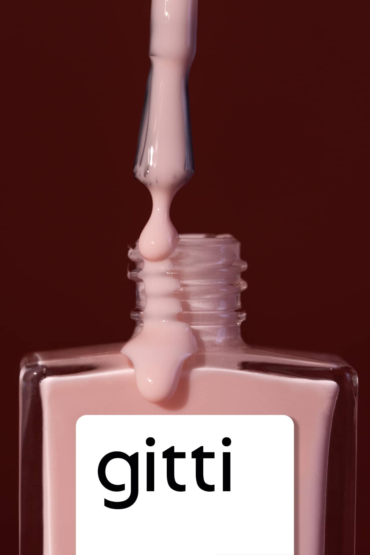 Ein Pinsel mit Nail Tint in einem milchig blassrosa Farbton tropft über den offenen Hals einer Flasche mit der Aufschrift gitti vor einem dunklen Hintergrund.