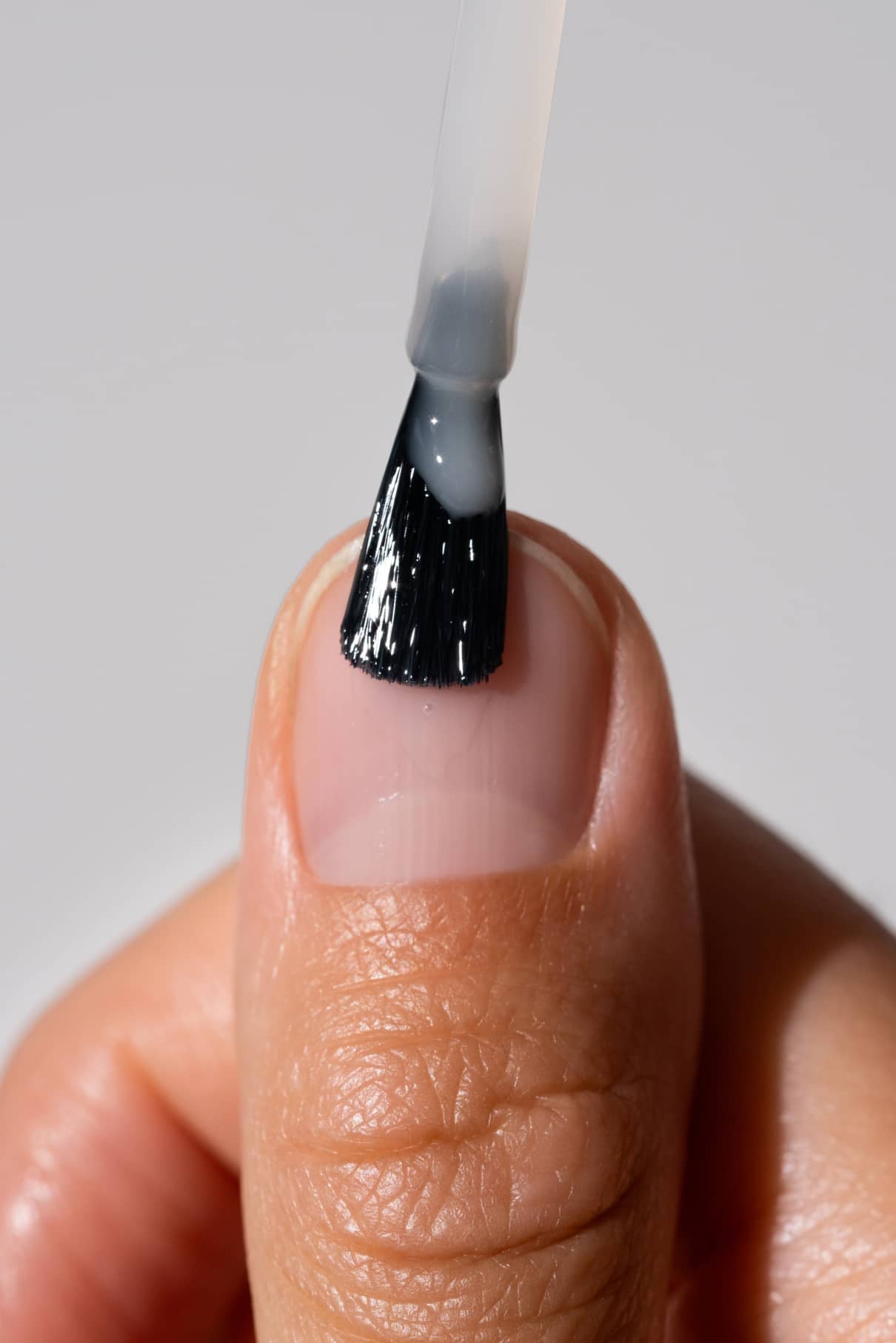 Nahaufnahme einer Hand, die den Smoothing Nail Primer mit einem Pinsel auf einen Fingernagel aufträgt - ein wesentlicher Schritt in der Nagelpflege, um die Nägel zu glätten und die Haftung der Farbe zu verbessern.