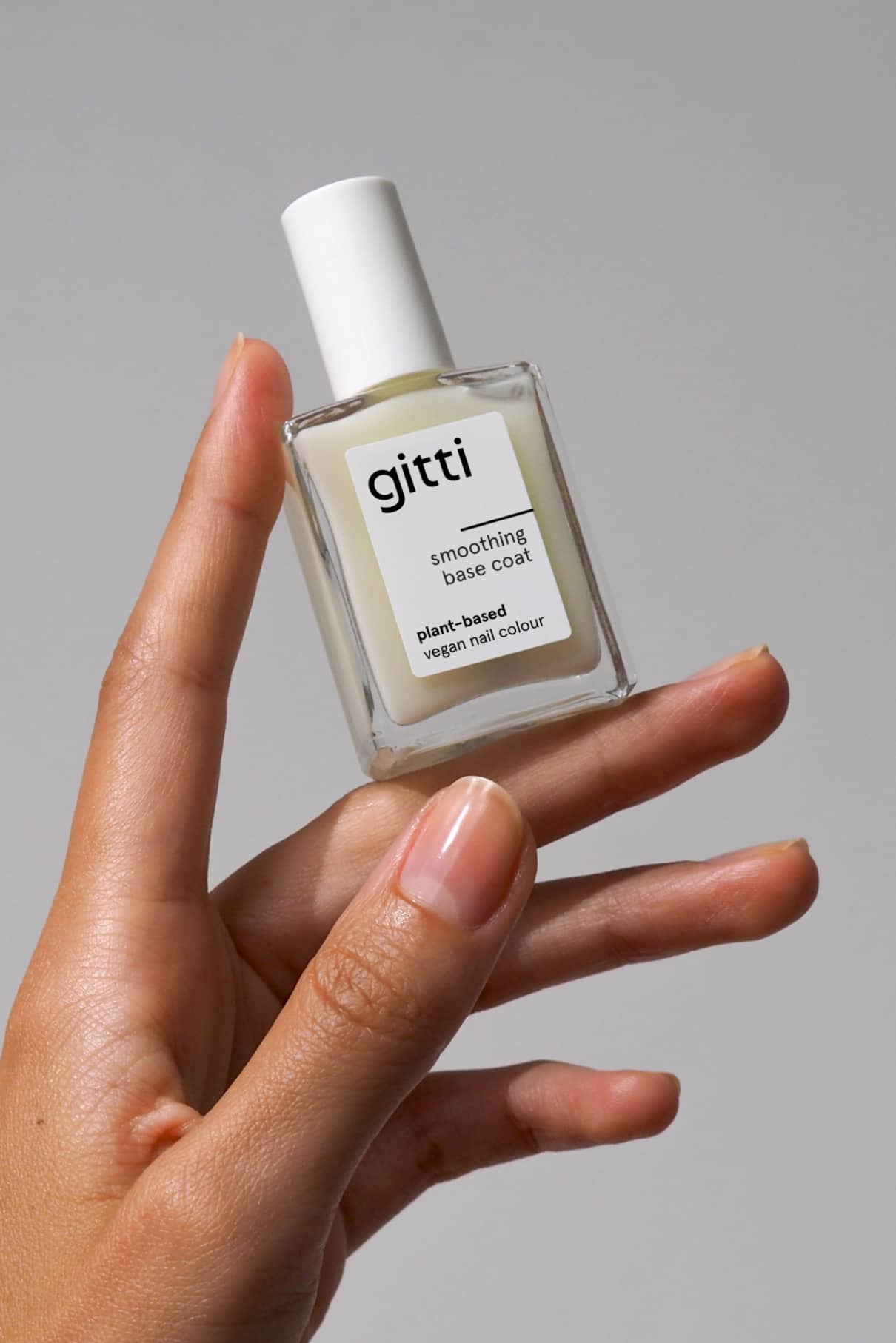 Eine Hand hält eine Flasche Infinite Gloss Duo, einen veganen Nagellack auf Pflanzenbasis, vor einem schlichten grauen Hintergrund.