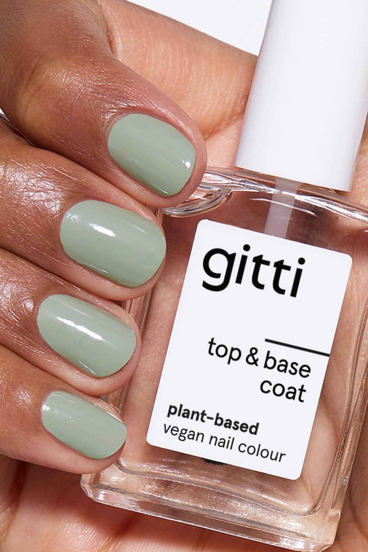 Eine Hand mit hellgrün lackierten Nägeln hält eine Flasche Plant-based Top&Base Coat, ein 2in1-Produkt für vegane Nagelfarbe, das zusätzlichen Halt und Glanz bietet.