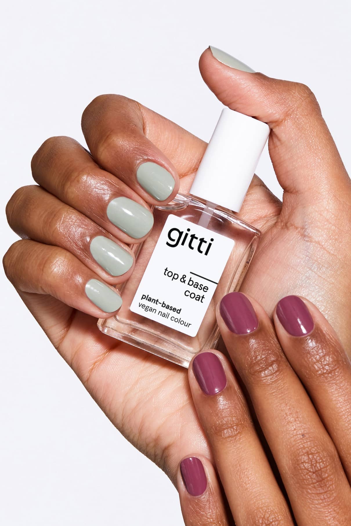 Eine Hand hält eine Flasche Top&Base Coat Nagellack auf pflanzlicher Basis, die Nägel sind salbeigrün und lila lackiert und bieten zusätzlichen Halt und Glanz für eine makellose Maniküre.
