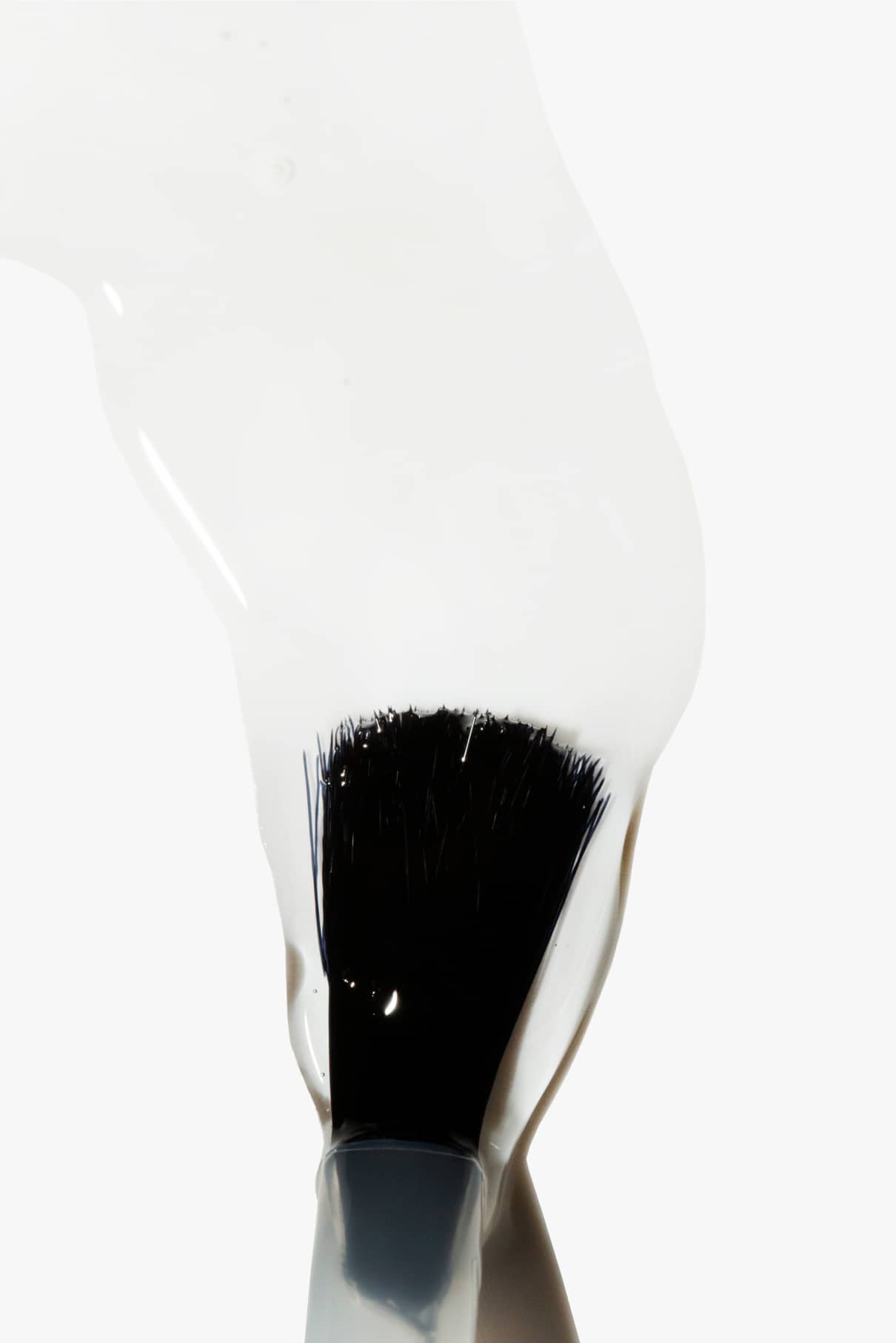 Eine Nahaufnahme eines Pinsels, der mit dickem, weißem Top&Base Coat auf Pflanzenbasis bestrichen ist, wobei das Glanz-Finish hervorgehoben wird, vor einem schlichten weißen Hintergrund.