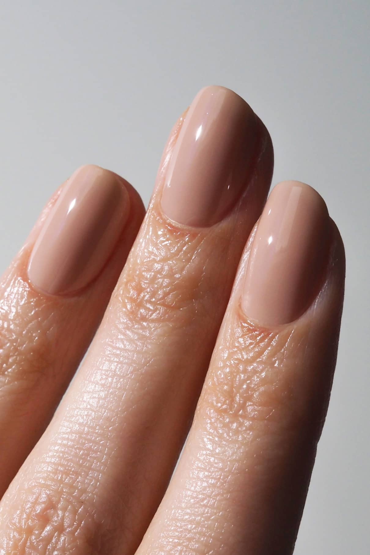 Nahaufnahme von drei Fingern mit kurzen, gepflegten Nägeln, lackiert in gitti no. 001, ein glänzender Beige-Ton für einen eleganten, natürlichen Look.