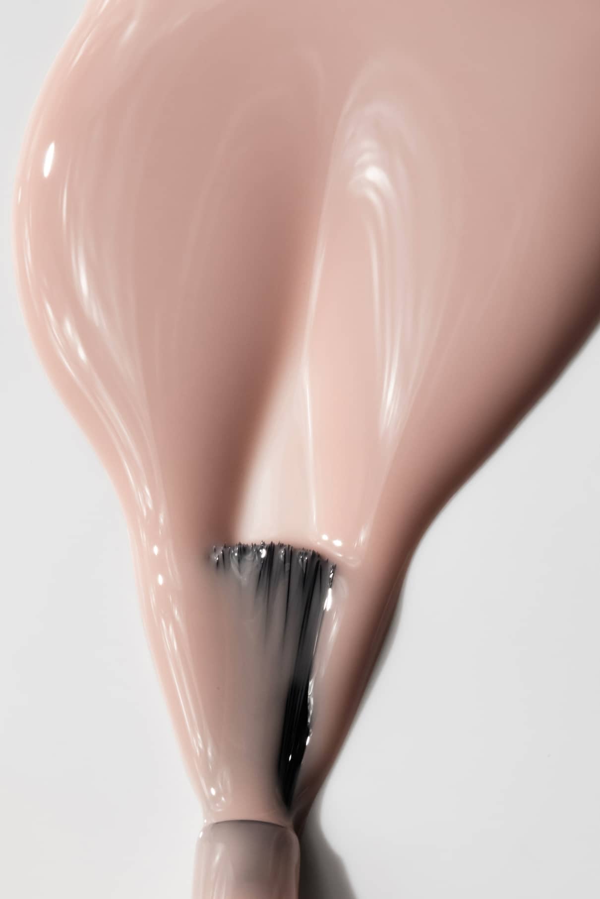 Nahaufnahme eines Pinsels, mit dem gitti no. 001, ein glänzender beiger Nagellack, in einer glatten Schicht auf eine weiße Oberfläche aufzutragen, wobei die Eleganz des glänzenden Beigetons hervorgehoben wird.