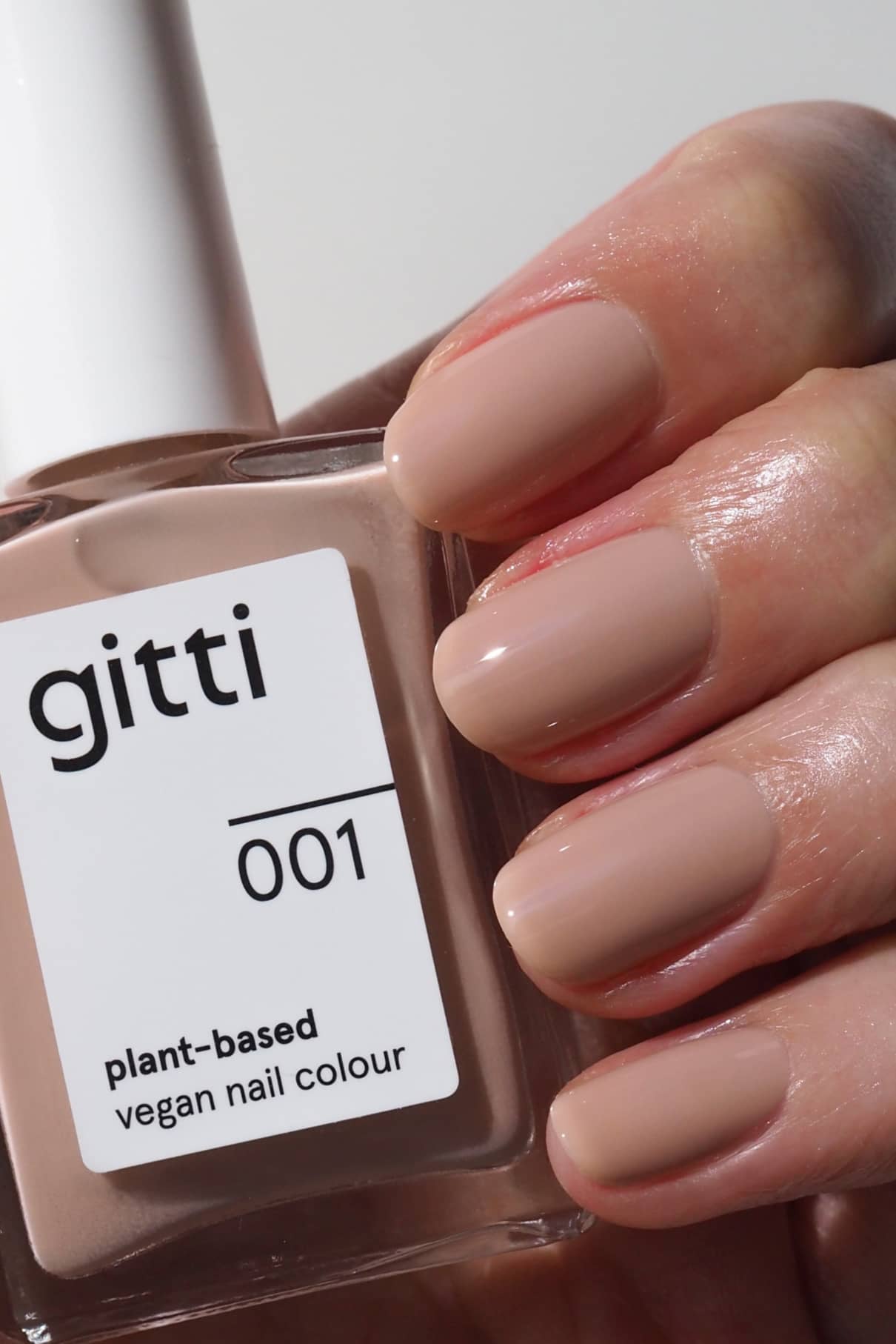 Eine Hand mit sauber manikürten Nägeln in einem glänzenden Beige-Ton hält eine Flasche gitti no. 001 pflanzlichen, veganen Nagellack.