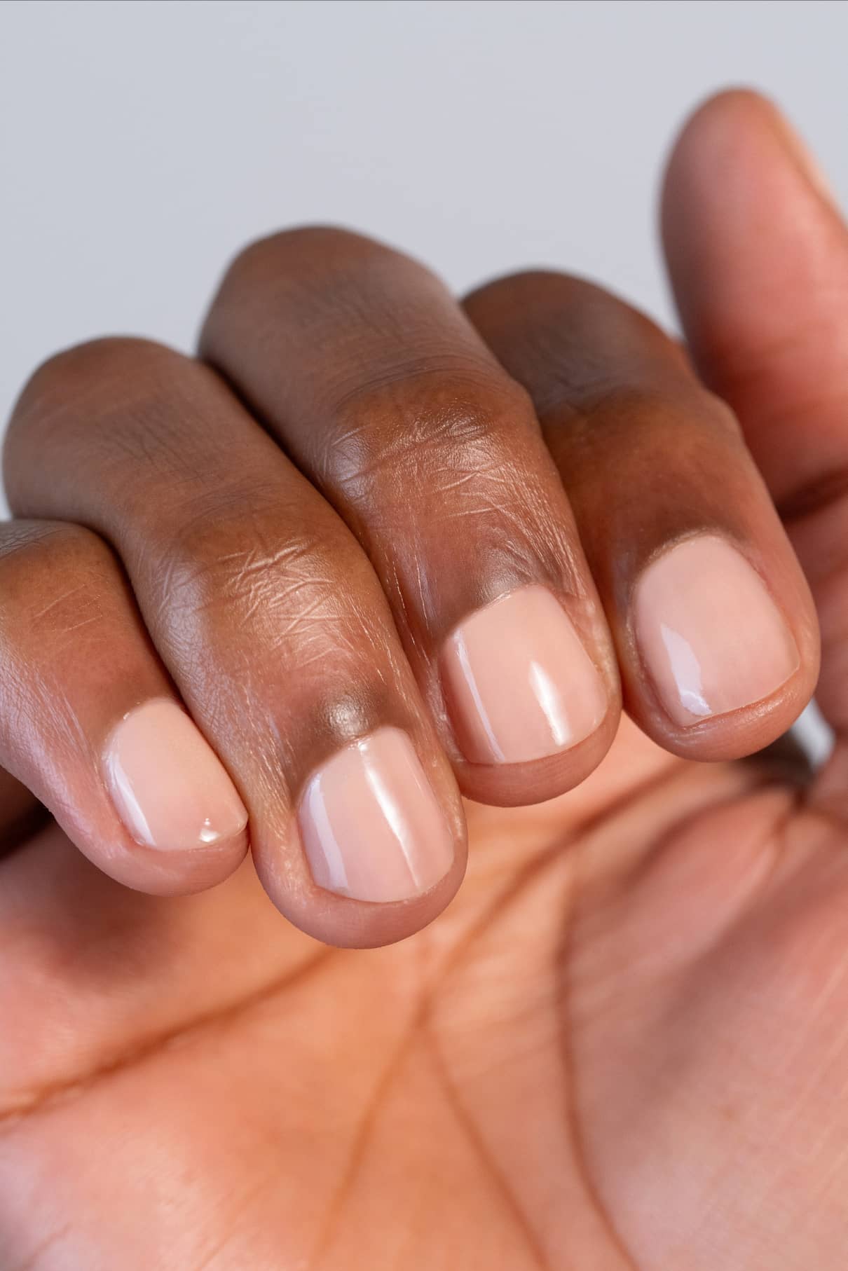 Eine Nahaufnahme einer Hand mit kurzen, ordentlich manikürten Nägeln, die in gitti no. 002, einem sanften Pfirsichton, inspiriert von der Pantone-Farbe des Jahres 2024. Ein Nagel hat einen subtilen dunklen Fleck in der Nähe der Nagelhaut.