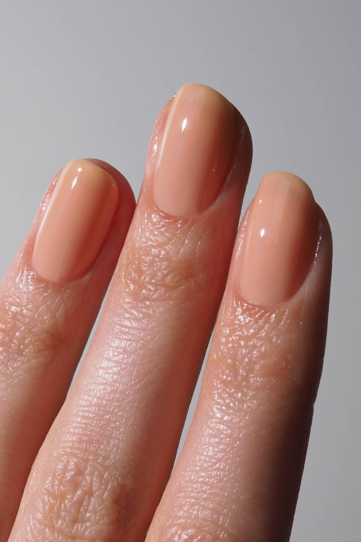 Nahaufnahme von drei Fingern mit sauber manikürten, ovalen Nägeln, die in glänzendem Gitti Nr. 002, inspiriert von Pantone Color of the Year 2024, vor einem neutralen Hintergrund.