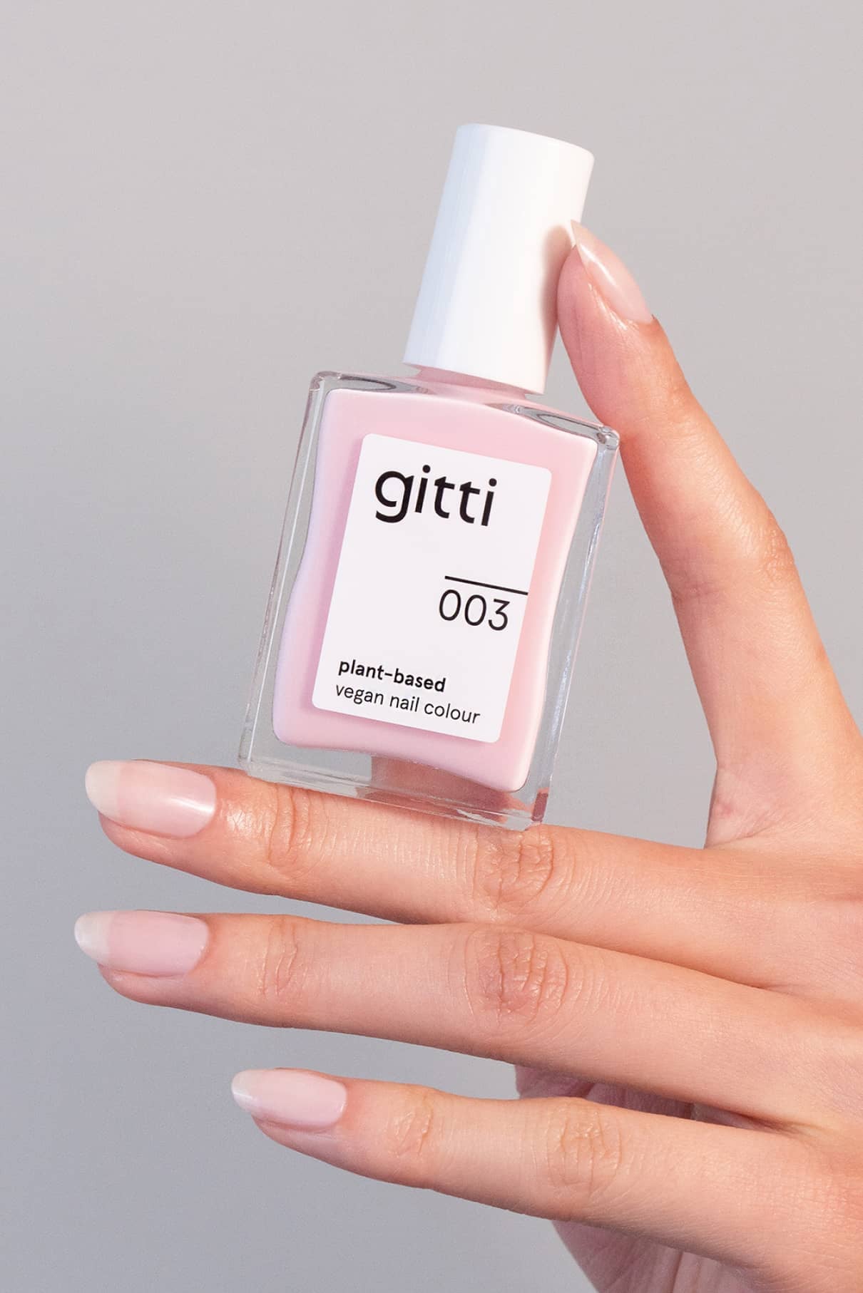 Eine Hand mit manikürten Nägeln hält eine Flasche mit gitti no. 003, einer pflanzlichen, veganen Nagelfarbe in einem zarten Rosaton.
