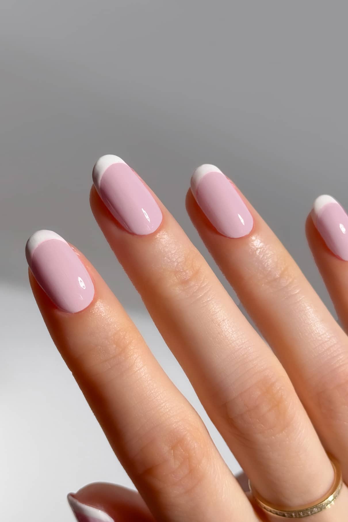 Eine Hand mit sauber manikürten Nägeln, lackiert mit gitti no. 003 in zartem Rosa und klassisch weißen French Tips vor einem neutralen Hintergrund.