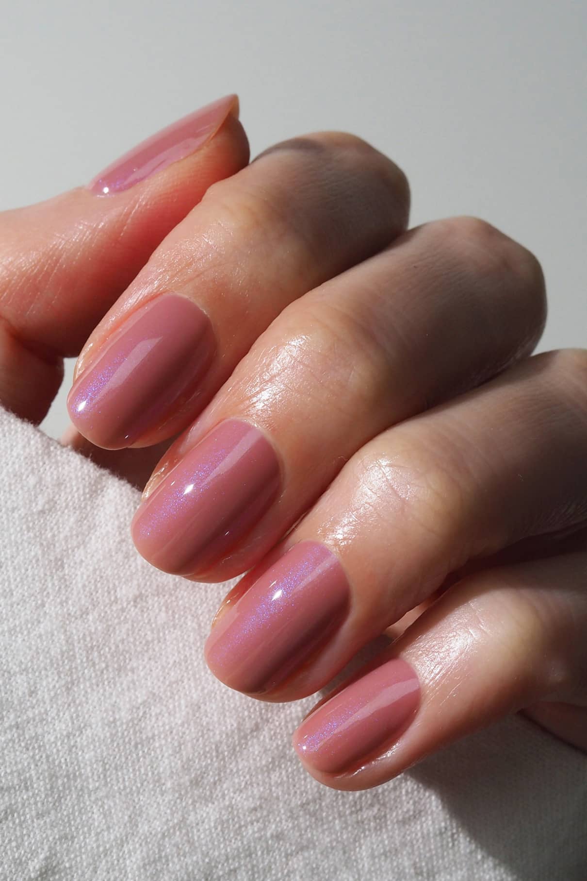 Eine Hand mit kurzen, ovalen Nägeln, die mit gitti no. 004, einem seidigen Mauve-Ton-Lack, hält einen weißen Stoff.