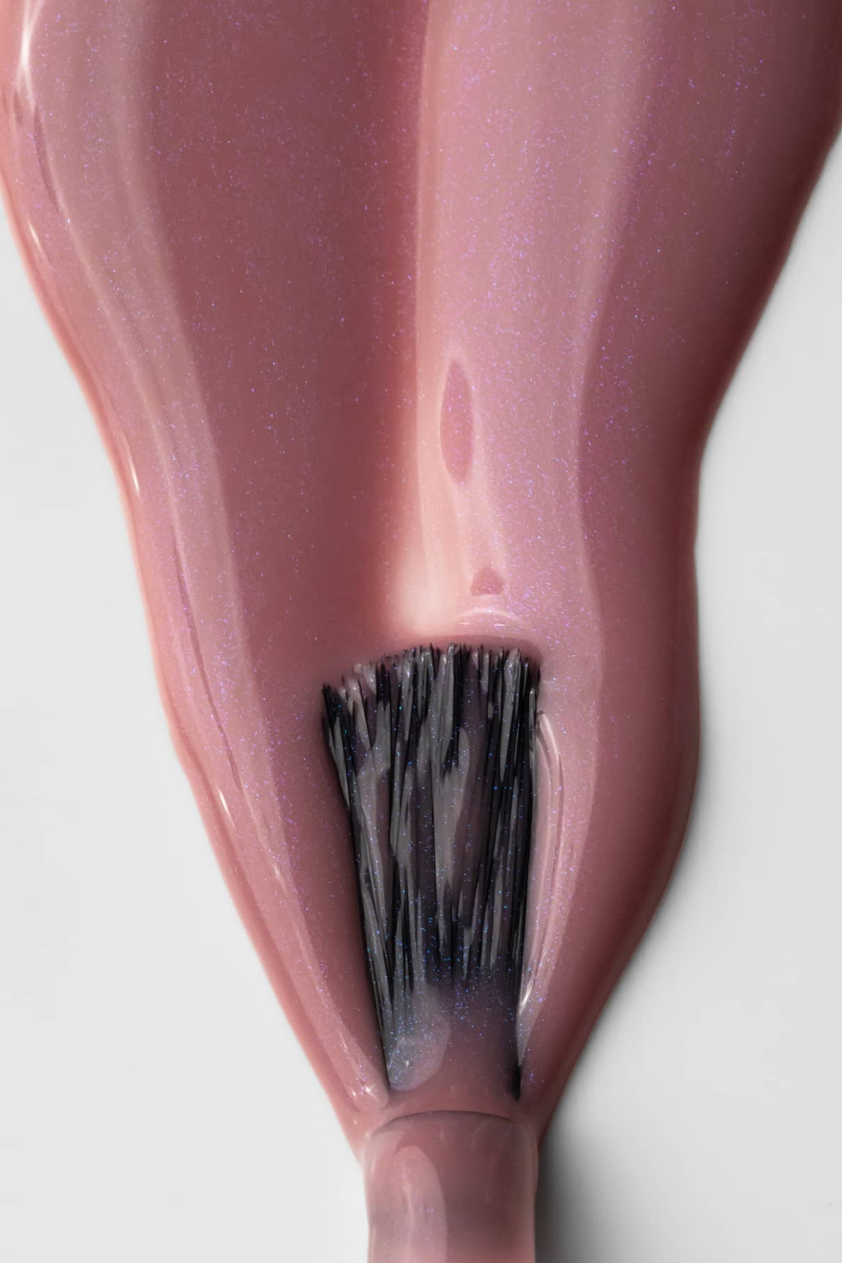 Nahaufnahme eines Nagellackpinsels, der gitti no. 004, ein schimmernder rosa Lack in einem seidigen Mauve-Ton, auf eine glatte Oberfläche.