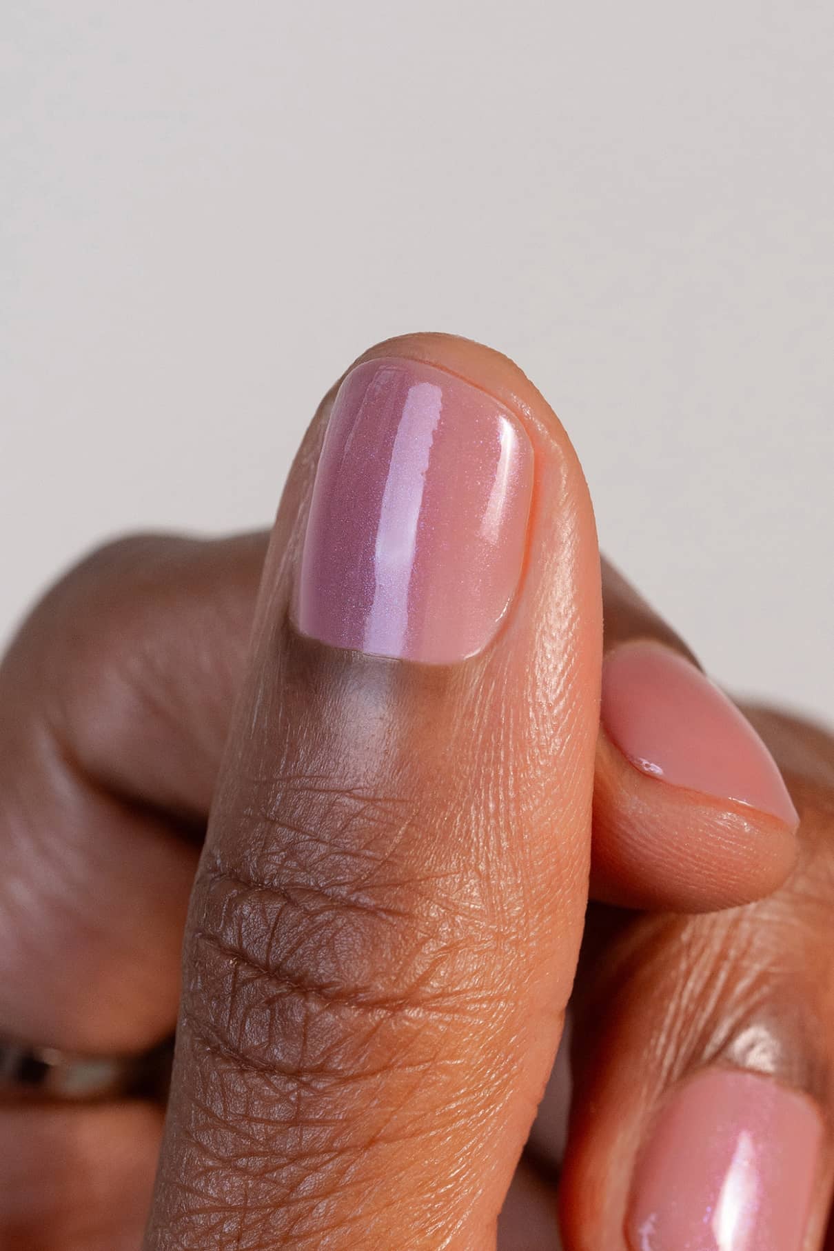 Nahaufnahme einer Hand mit Naturnägeln, die in dem glänzenden, seidenmatten Farbton gitti no. 004, wobei der Daumen vor einem unifarbenen Hintergrund in den Fokus gerückt wird.
